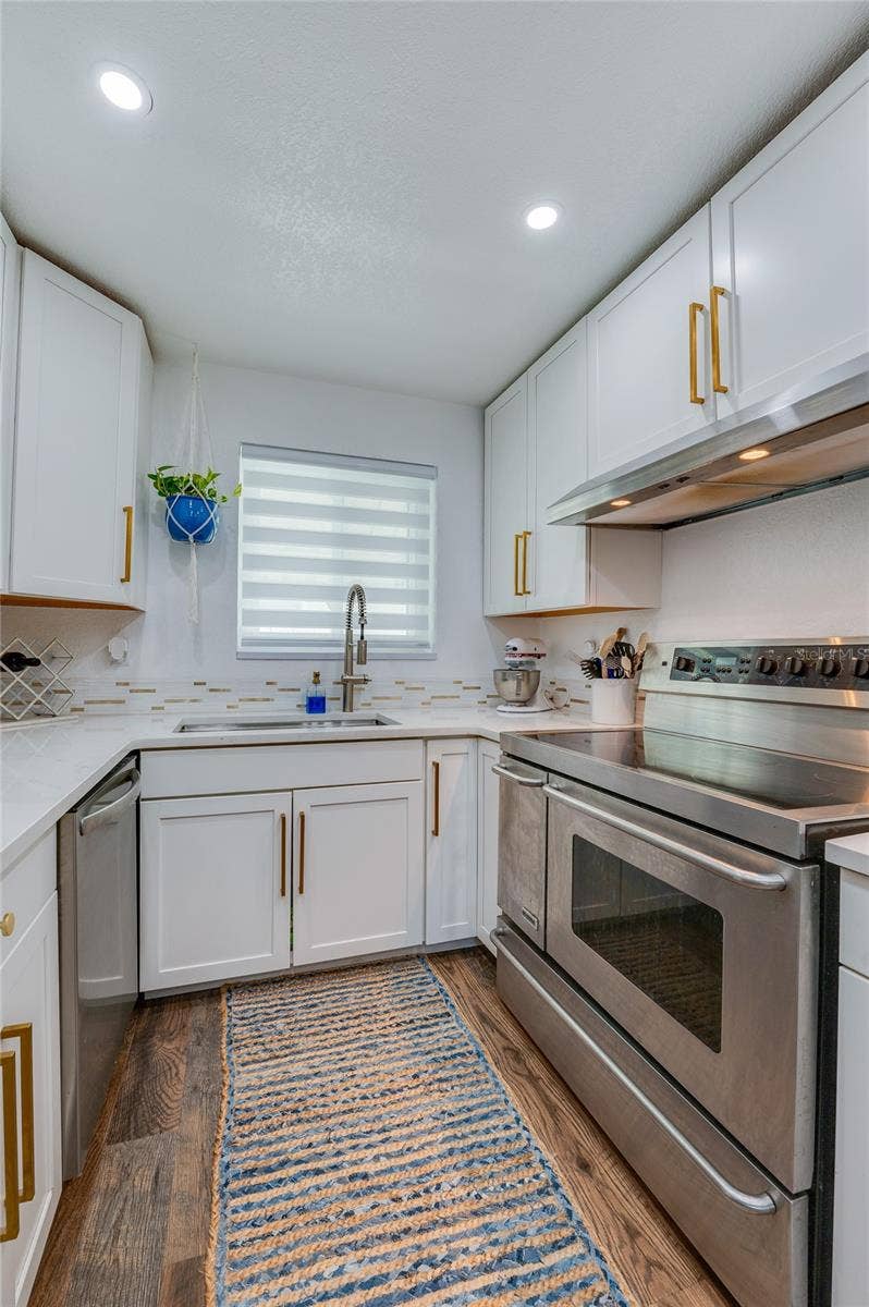 348 WOODLAND AVENUE, Daytona Beach, FL 32118 Functional kitchen workspace displaying full-size stainless steel appliances, modern quartz counters, and a window above the deep sink.