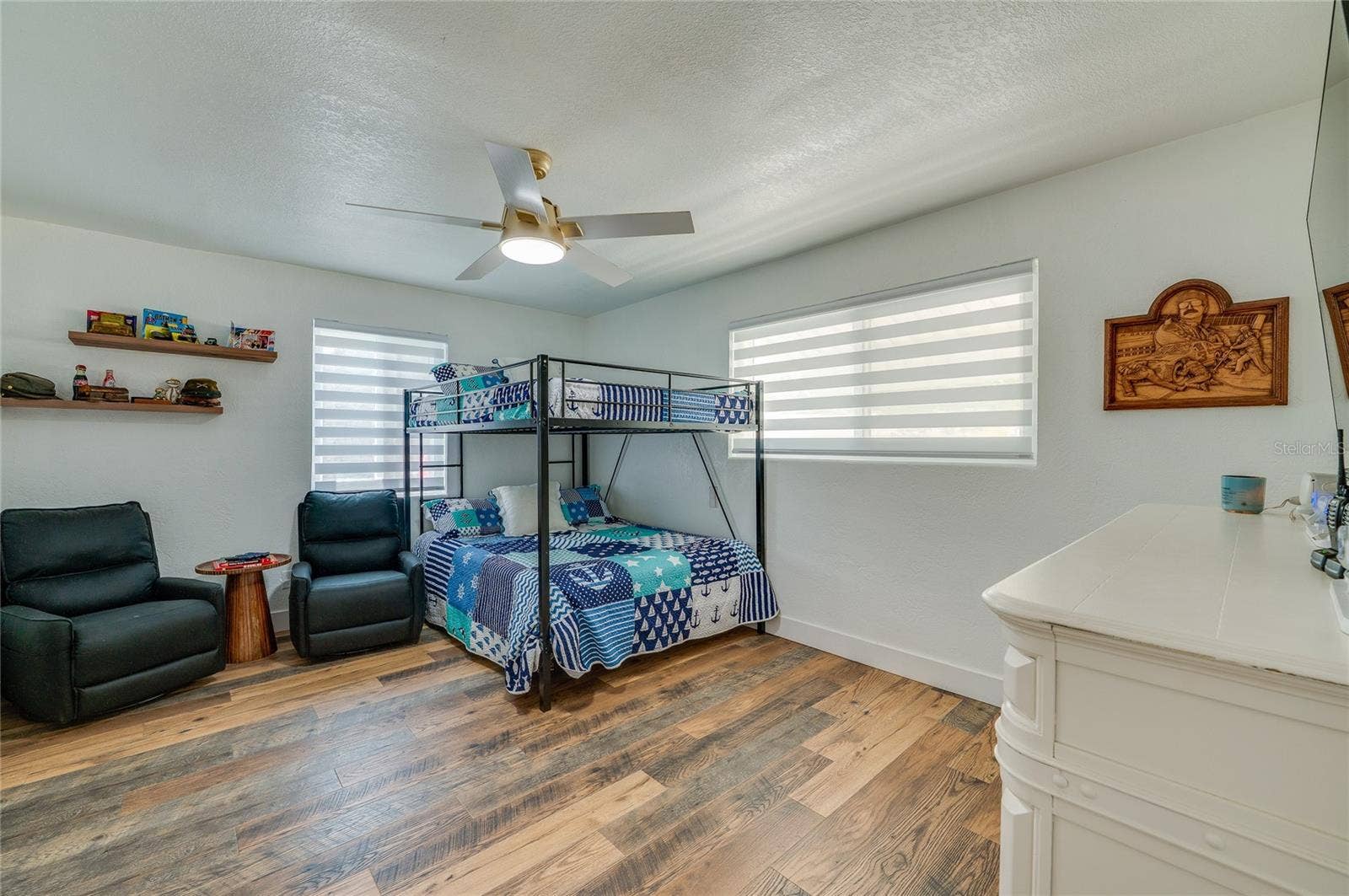 348 WOODLAND AVENUE, Daytona Beach, FL 32118 Generous bedroom design highlighting warm LVP flooring, neutral walls, two large windows with blinds, and floating display shelves.