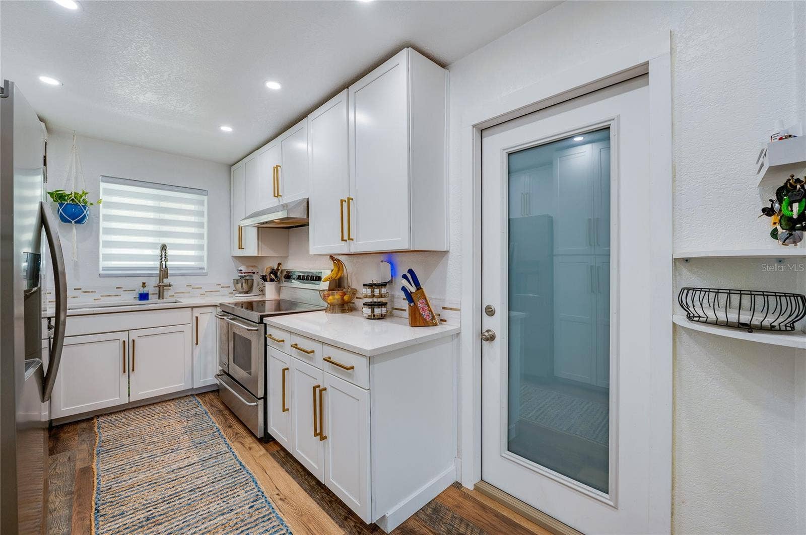 348 WOODLAND AVENUE, Daytona Beach, FL 32118 Sleek kitchen space complete with white cabinetry, warm LVP flooring, stainless steel appliances, and a glass-paneled door.