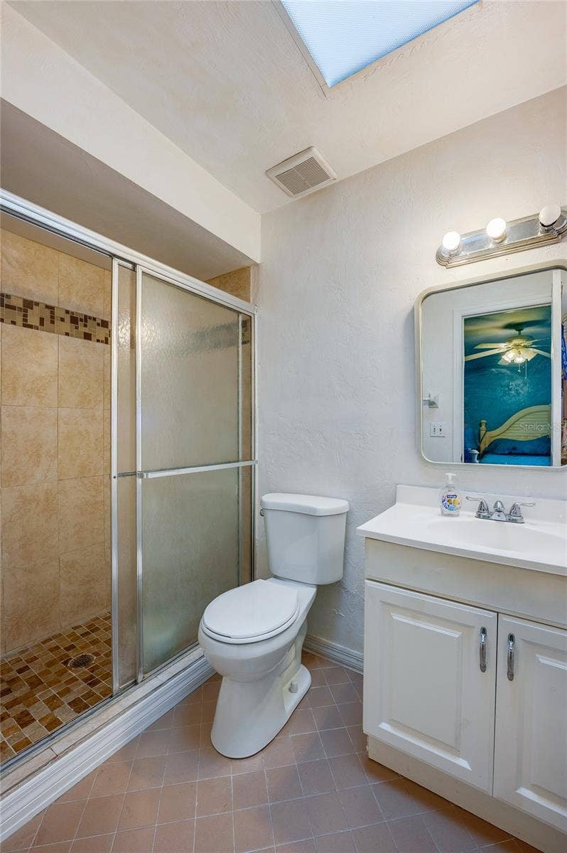 146 WESTWOOD DRIVE, Daytona Beach, FL 32119 Ensuite bathroom featuring a walk-in shower with tiled surround and glass sliding doors, paired with a white vanity and skylight overhead.