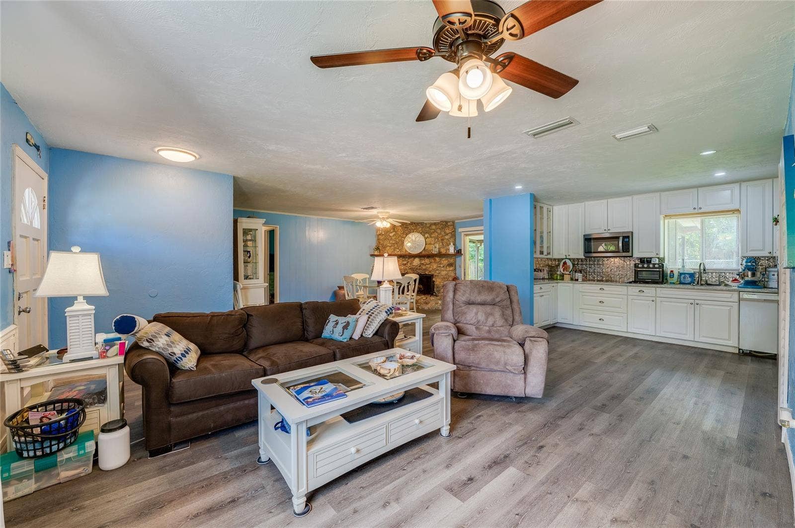 146 WESTWOOD DRIVE, Daytona Beach, FL 32119 Bright open-concept living area with LVP flooring, cool blue walls, and a ceiling fan leading into the adjacent kitchen and dining spaces.