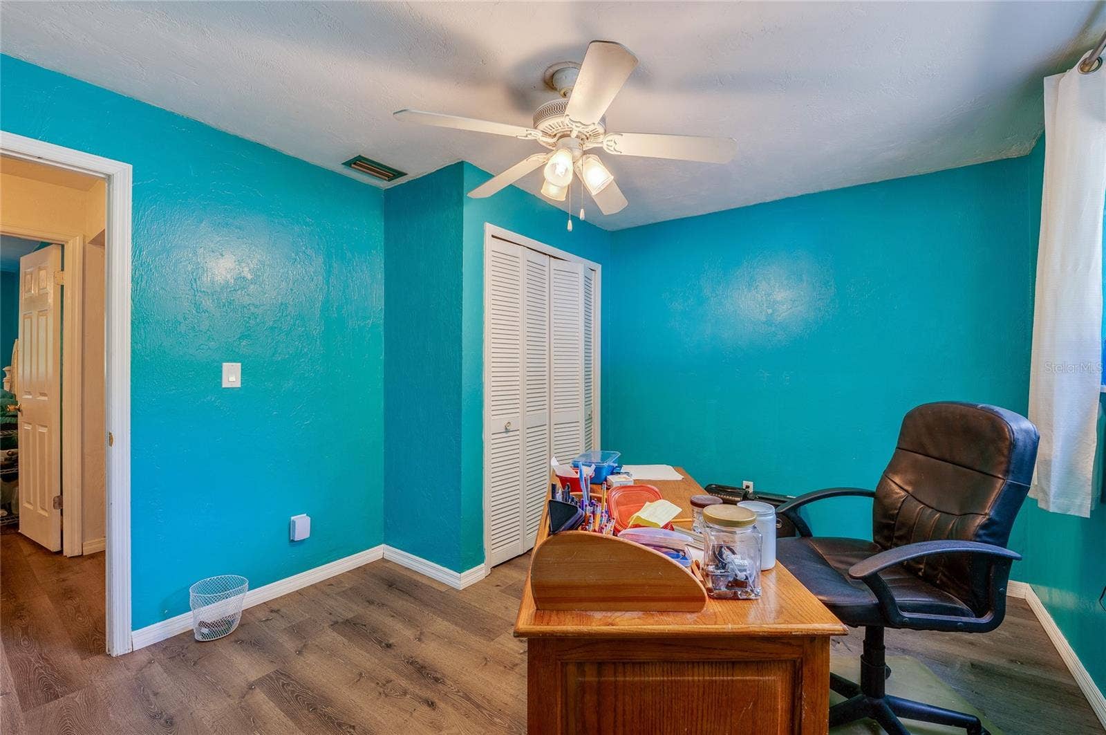 146 WESTWOOD DRIVE, Daytona Beach, FL 32119 Functional home office/bedroom area illuminated by a ceiling fan, featuring turquoise walls, closet storage, and durable LVP flooring.