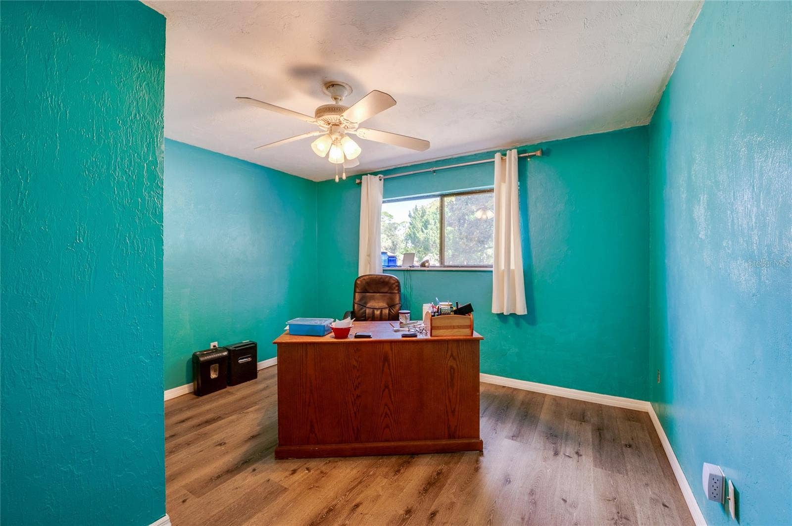 146 WESTWOOD DRIVE, Daytona Beach, FL 32119 Spacious home office/bedroom featuring vibrant teal walls, low-maintenance LVP flooring, and a large window providing ample natural light.