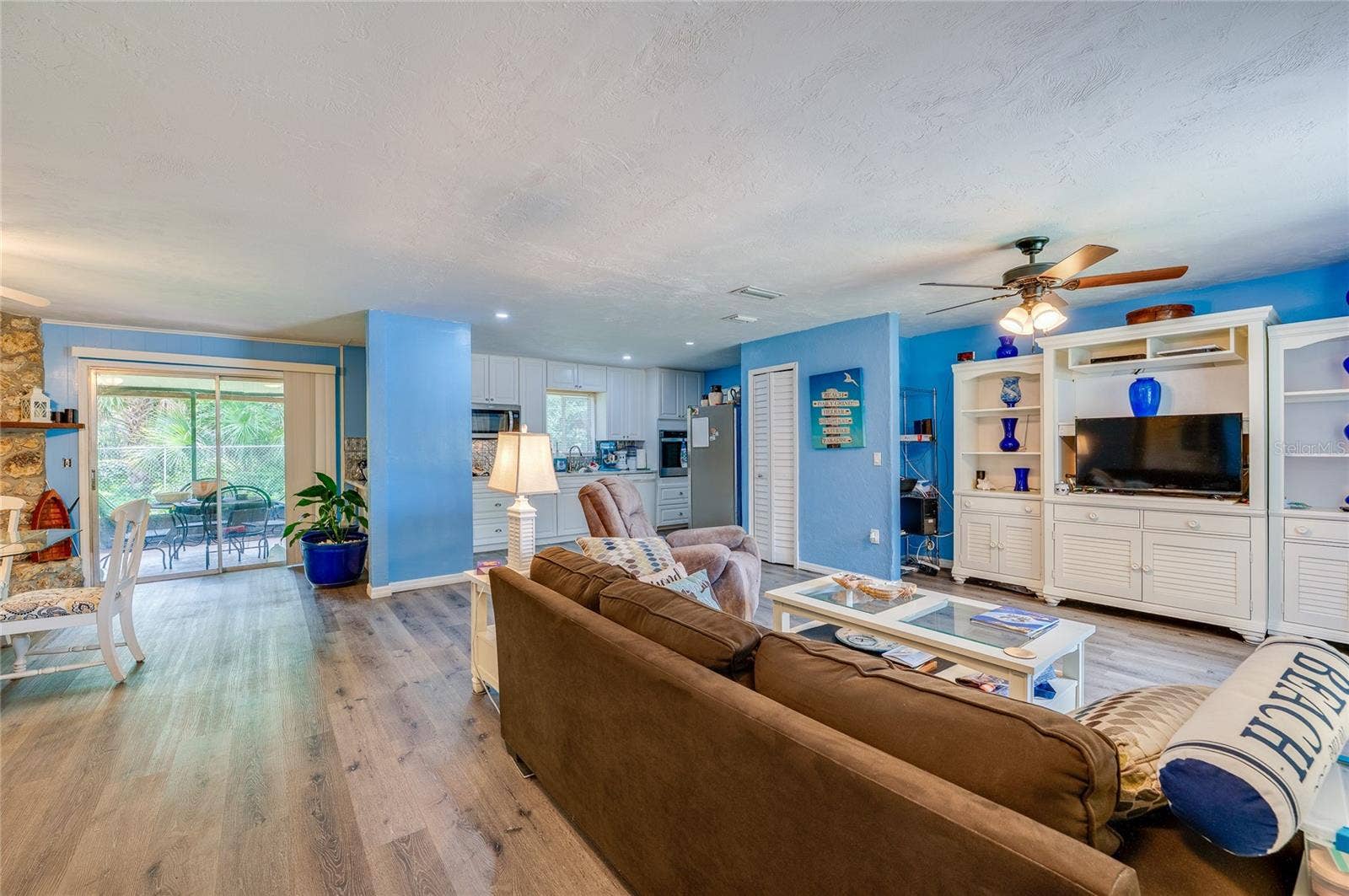146 WESTWOOD DRIVE, Daytona Beach, FL 32119 Expansive open living space featuring LVP flooring, bright blue walls, and a large built-in media center. Sliding glass doors open to the adjacent screened patio area.