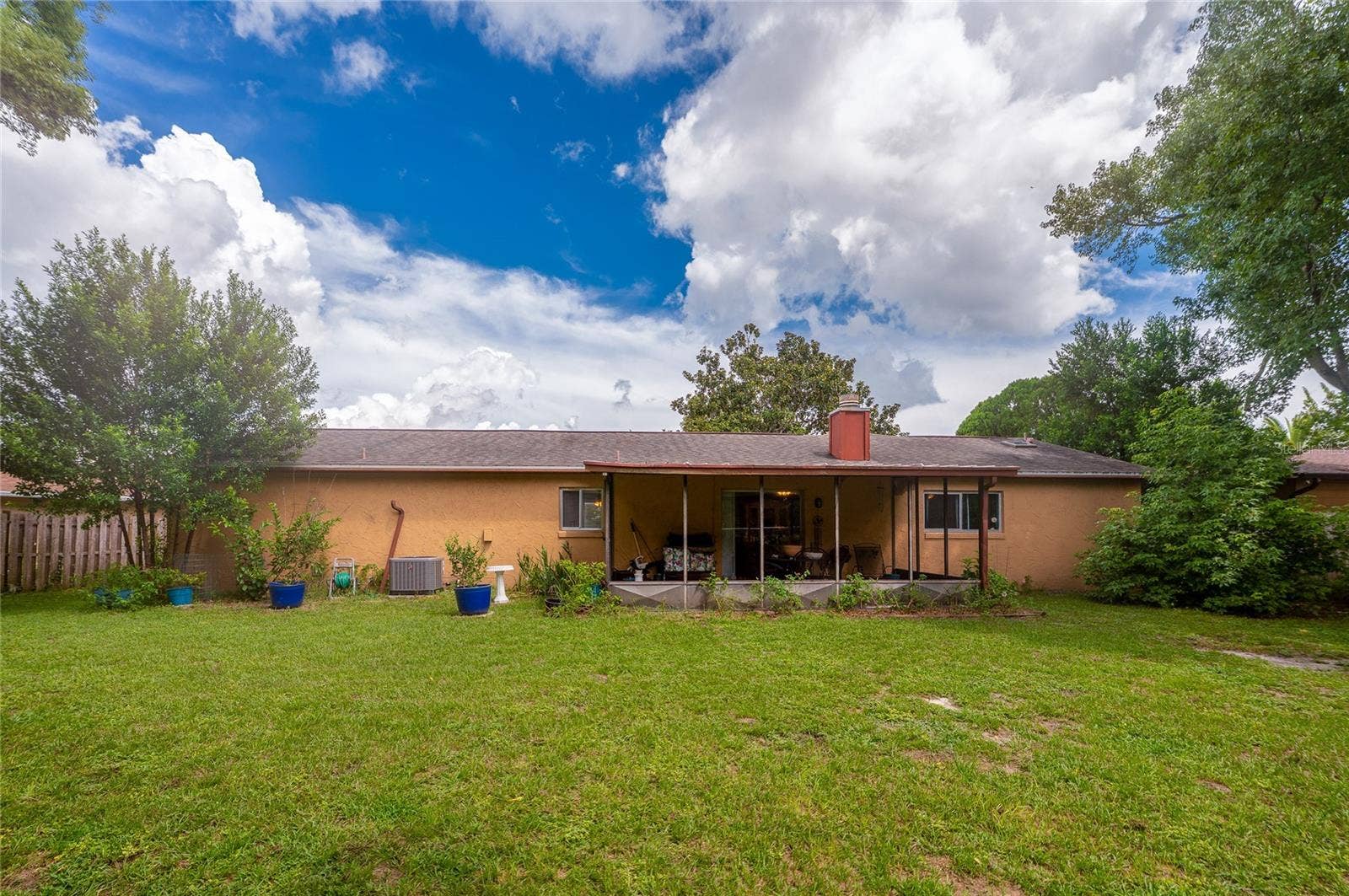 146 WESTWOOD DRIVE, Daytona Beach, FL 32119 Rear view of the single-story home featuring a screened back patio, exterior HVAC unit, potted plants, and a spacious green lawn.