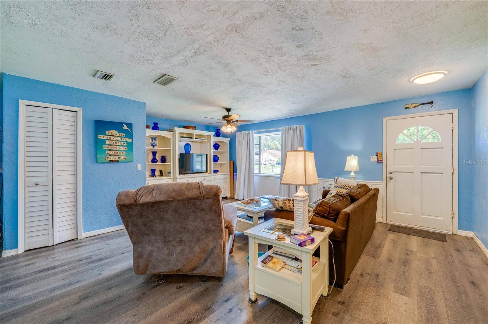 146 WESTWOOD DRIVE, Daytona Beach, FL 32119 Open living space featuring light blue walls, LVP flooring, double closets, and a white front entry door with glass pane accents.