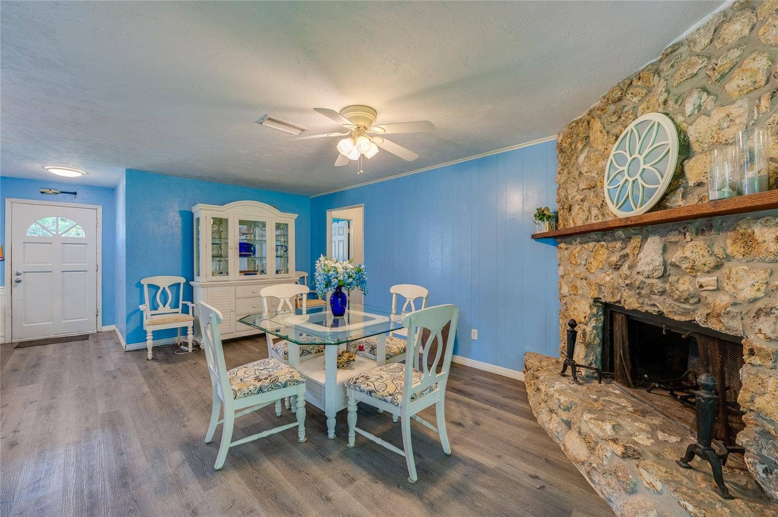 146 WESTWOOD DRIVE, Daytona Beach, FL 32119 Open-concept living room anchored by a rustic stone fireplace, featuring light blue walls, LVP flooring, and a lighted ceiling fan.