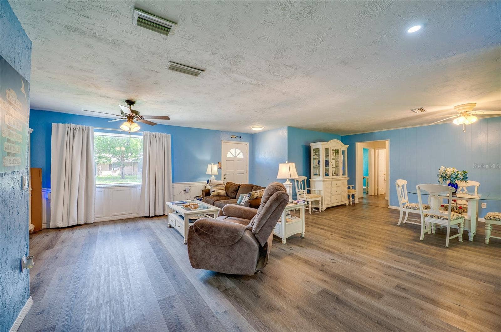146 WESTWOOD DRIVE, Daytona Beach, FL 32119 Spacious main living area displaying LVP flooring, light blue walls, a wide window bringing in natural light, and smooth transitions to adjoining rooms.