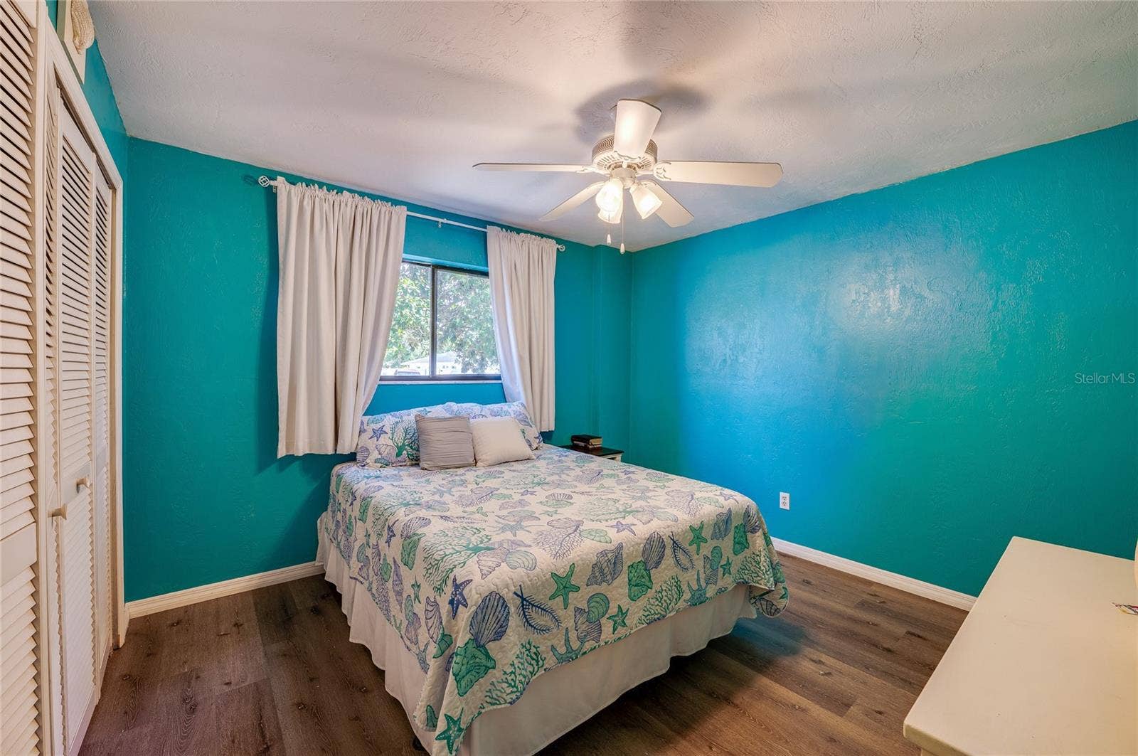 146 WESTWOOD DRIVE, Daytona Beach, FL 32119 Vibrant coastal-themed bedroom accented with bright turquoise walls, modern LVP flooring, and a ceiling fan. Double closet doors offer ample storage space.