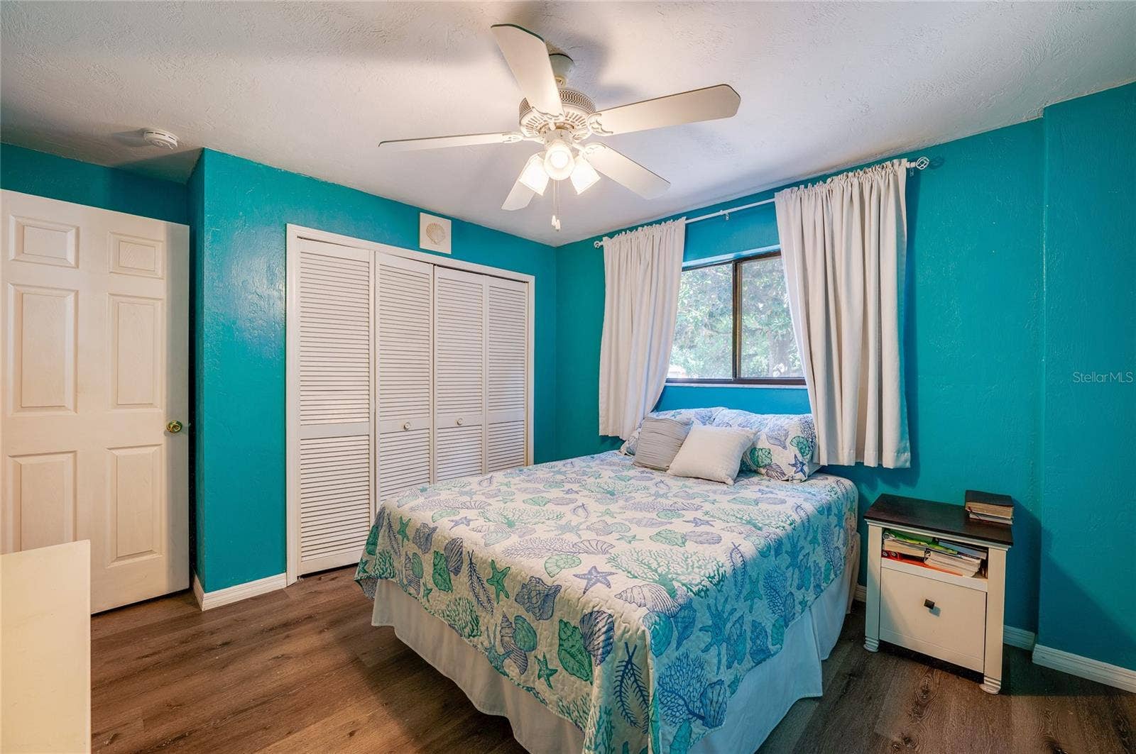 146 WESTWOOD DRIVE, Daytona Beach, FL 32119 Bright bedroom showcasing vibrant blue walls, light-toned LVP flooring, and double louvered closet doors under a classic white ceiling fan.