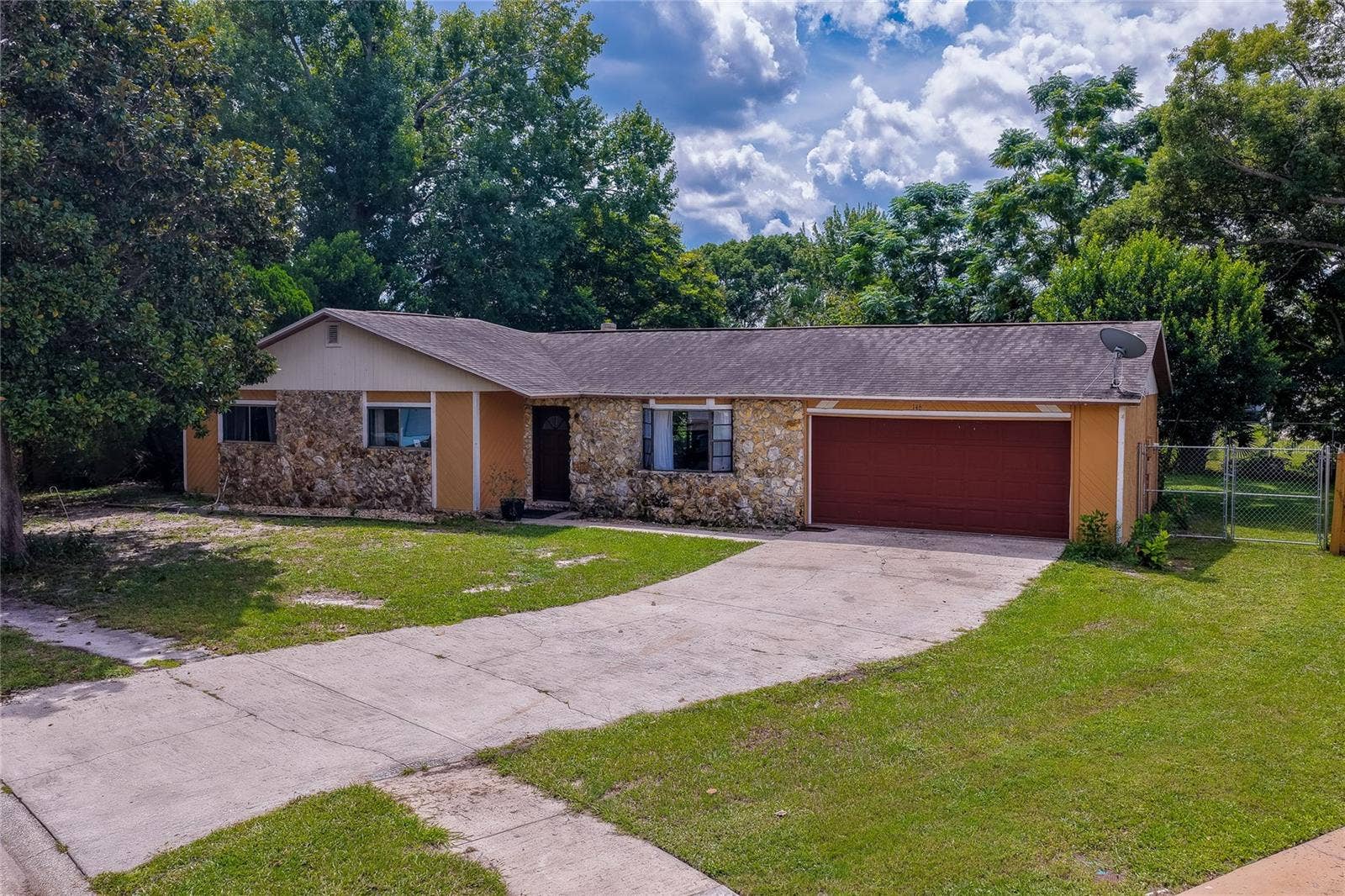 146 WESTWOOD DRIVE, Daytona Beach, FL 32119 Charming single-story ranch home featuring a stone-accented facade, attached two-car garage, and an expansive paved driveway framed by lush green lawns and mature trees.