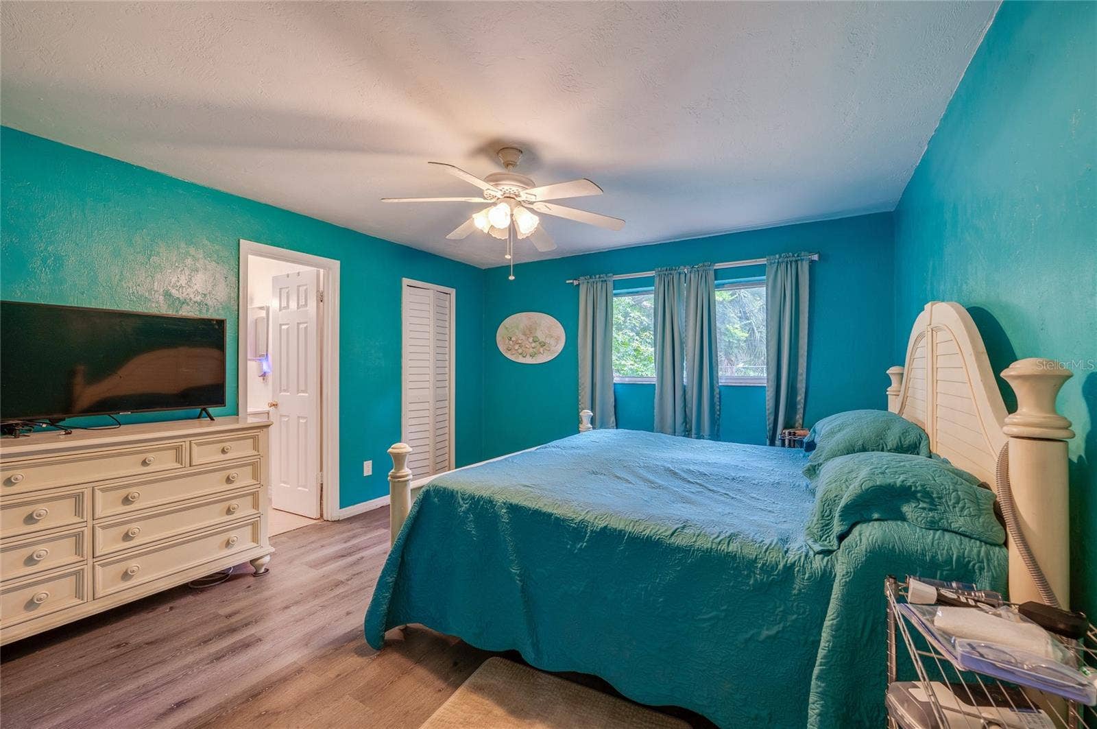146 WESTWOOD DRIVE, Daytona Beach, FL 32119 Primary bedroom suite styled with bright turquoise walls, LVP flooring, a white-panel closet, and direct access to an ensuite bathroom.