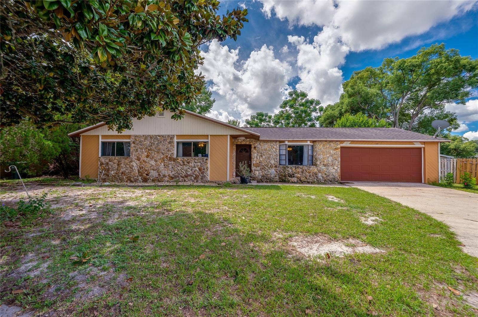 146 WESTWOOD DRIVE, Daytona Beach, FL 32119 Front exterior of the ranch-style house showcasing decorative stone accent walls, a red garage door, concrete driveway, and front lawn.