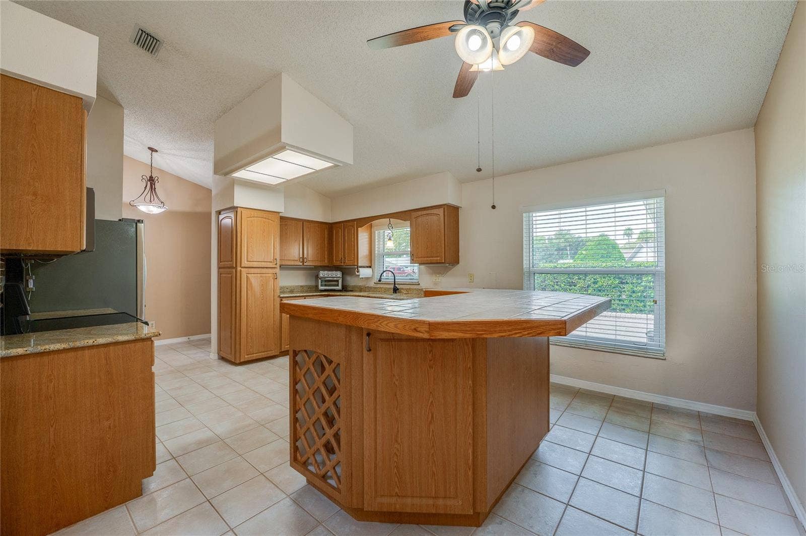 4669 SECRET RIVER TRAIL, Port Orange, FL 32129 Spacious kitchen displaying warm wooden cabinetry, a tiled center island with built-in wine storage, tile flooring, and a bright window over the sink.