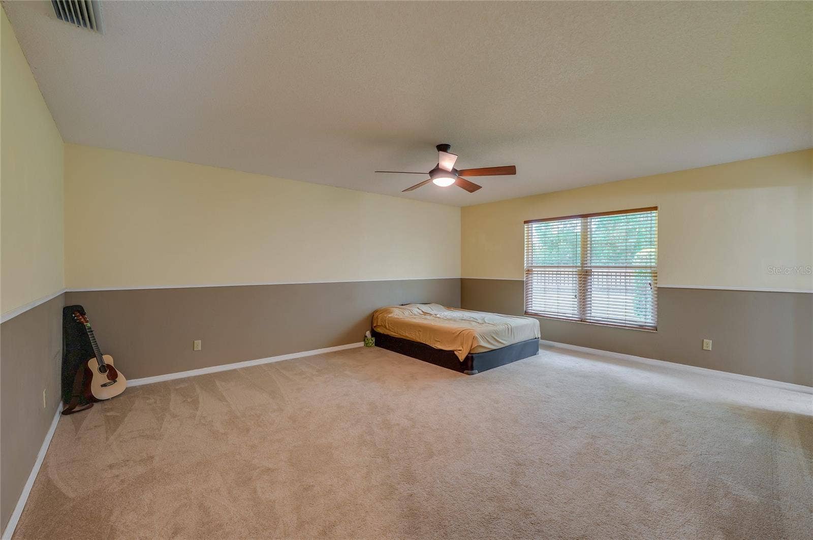 4669 SECRET RIVER TRAIL, Port Orange, FL 32129 Spacious primary bedroom featuring soft carpeting, two-tone painted walls, a central ceiling fan, and a large window providing pleasant outdoor views.
