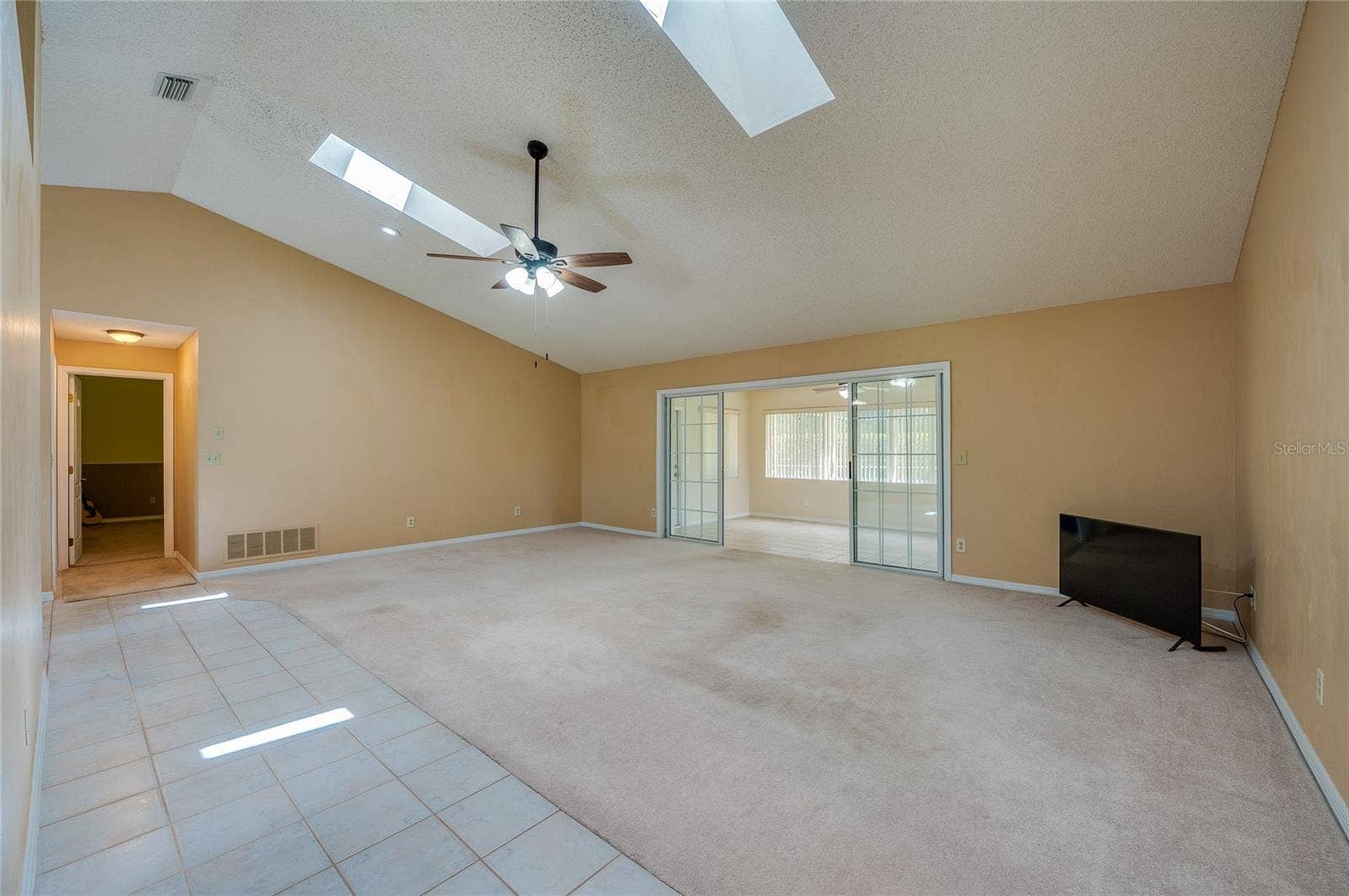 4669 SECRET RIVER TRAIL, Port Orange, FL 32129 Expansive living room area featuring vaulted ceilings with skylights, carpeted flooring, and sliding glass doors that open to a sun room.