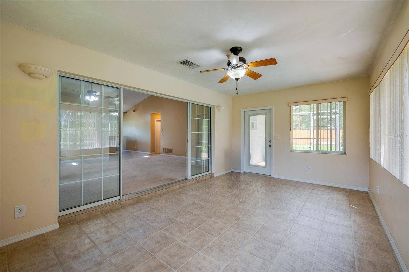 4669 SECRET RIVER TRAIL, Port Orange, FL 32129 Versatile sunroom space featuring sliding glass entry doors, tile flooring, a ceiling fan fixture, and a exterior door providing outdoor access.