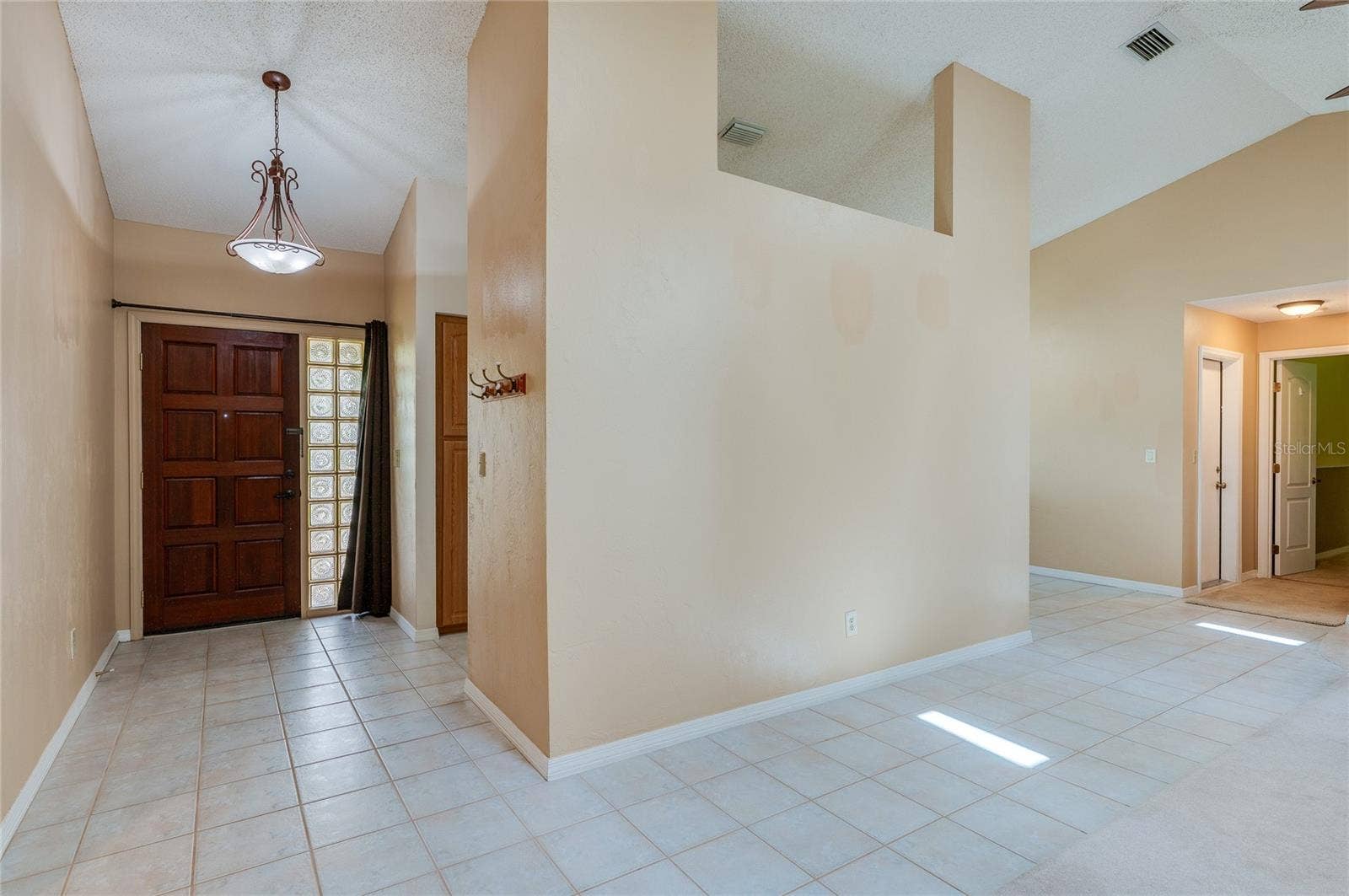4669 SECRET RIVER TRAIL, Port Orange, FL 32129 Spacious entry hallway featuring tile flooring, warm neutral walls, and a large decorative wood door with glass block side panels. Vaulted ceilings and open wall cutouts create a light-filled ambiance.