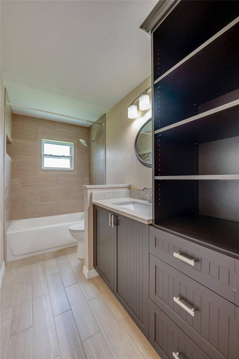 4669 SECRET RIVER TRAIL, Port Orange, FL 32129 Full bathroom with modern tile flooring, custom dark cabinetry, and open storage. A tiled tub-and-shower combo and elegant wall lighting complete the space.