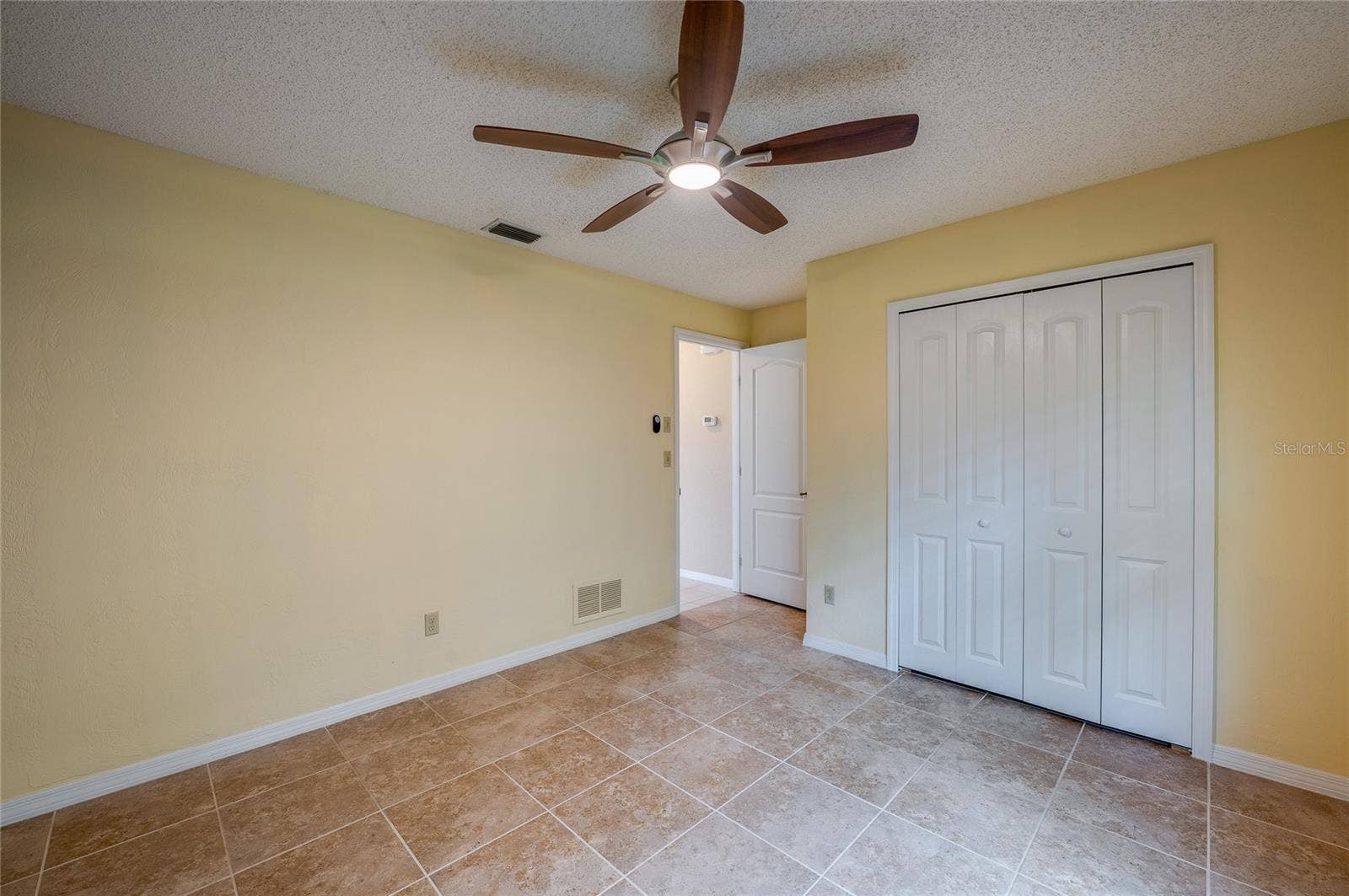 4669 SECRET RIVER TRAIL, Port Orange, FL 32129 Light-filled bedroom highlighting tiled flooring, smooth neutral walls, and double closet doors for storage. Ceiling fan fixture ensures comfortable airflow.