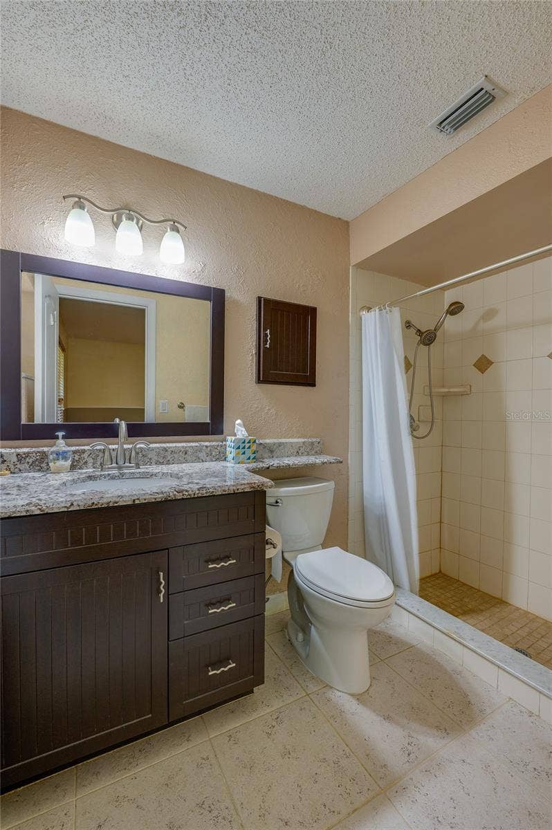 4669 SECRET RIVER TRAIL, Port Orange, FL 32129 Primary bathroom showcasing a dark wood vanity with granite countertops, tiled flooring, a wide framed mirror, and a walk-in tiled shower.