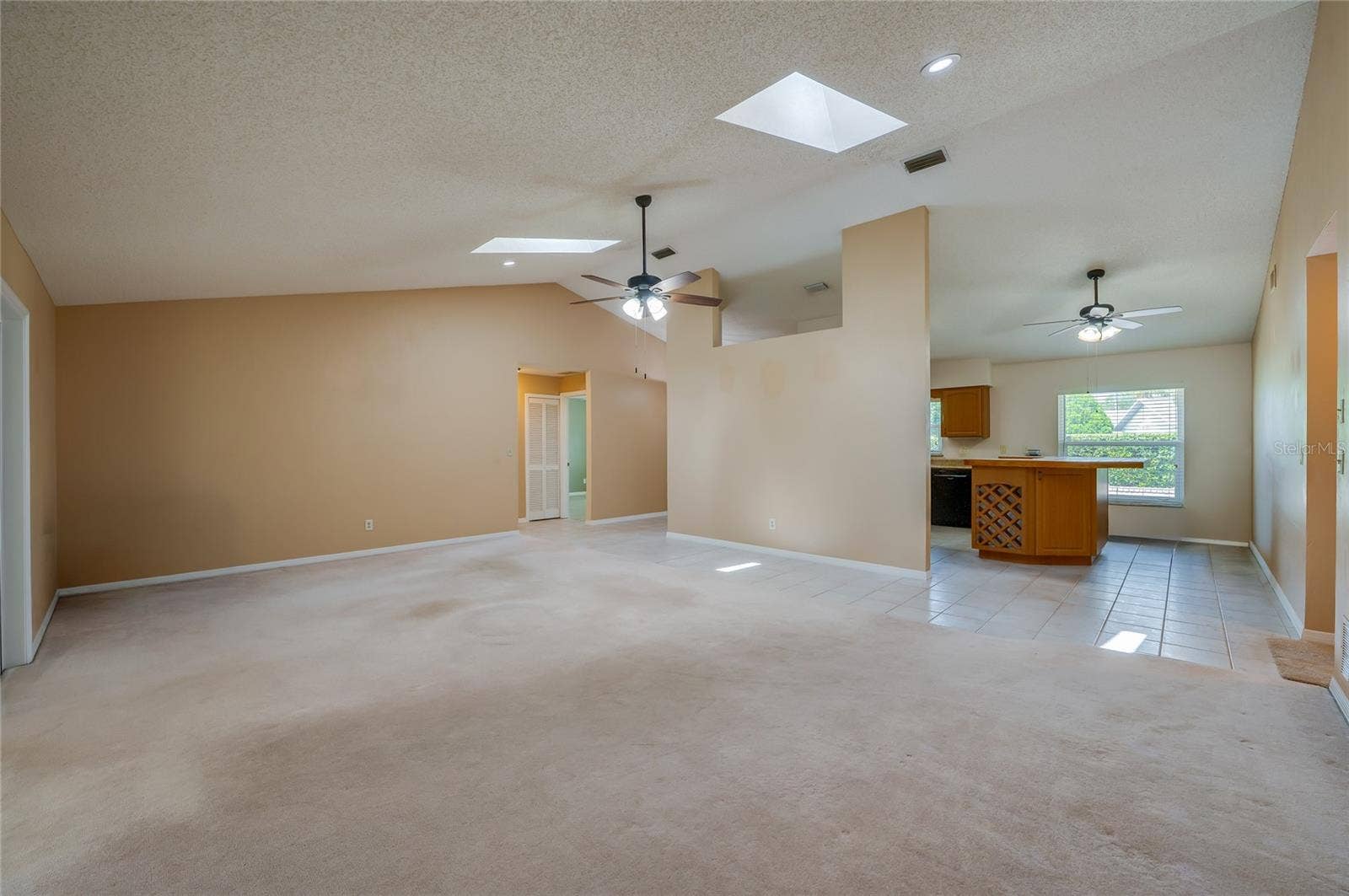 4669 SECRET RIVER TRAIL, Port Orange, FL 32129 Open-concept living space highlighting high vaulted ceilings, skylights, plush carpeting, and seamless flow into the adjacent tiled kitchen area.
