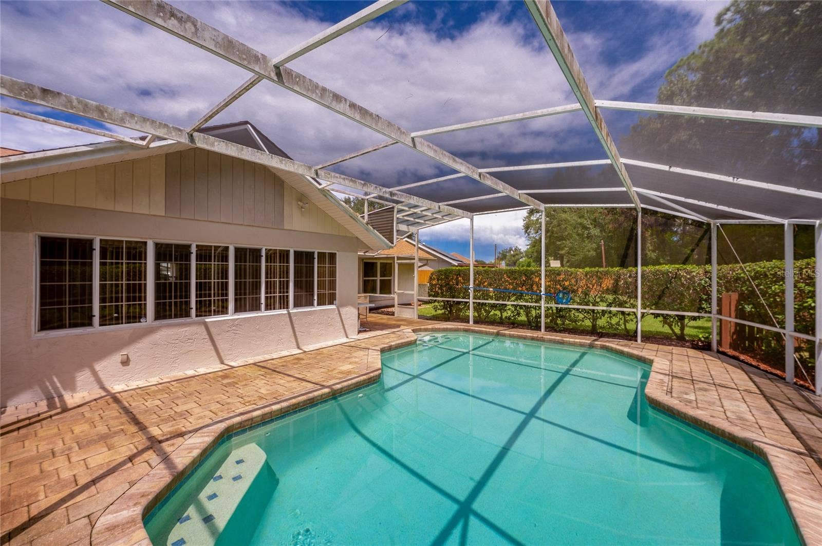 4669 SECRET RIVER TRAIL, Port Orange, FL 32129 Alternate angle of the screened swimming pool enclosure, highlighting the extensive paved deck and home exterior.
