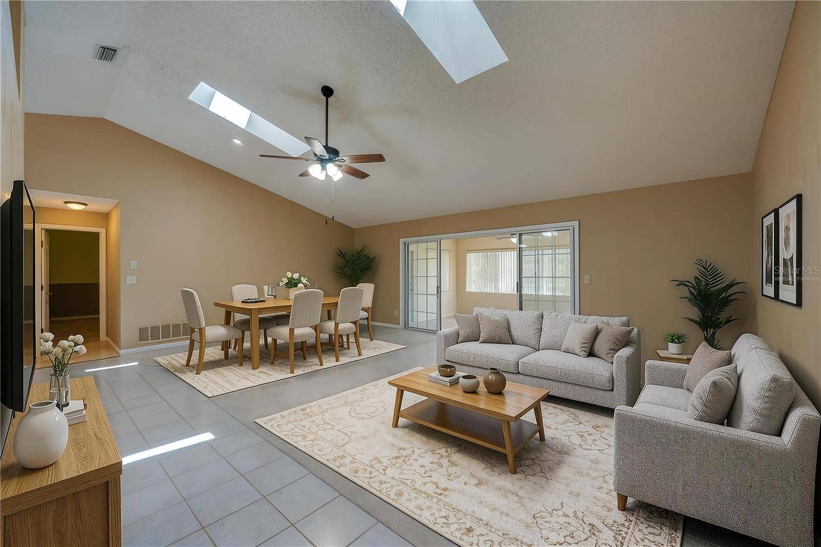 4669 SECRET RIVER TRAIL, Port Orange, FL 32129 Virtually Staged - Expansive living room area featuring vaulted ceilings with skylights, carpeted flooring, and sliding glass doors that open to a sun room.