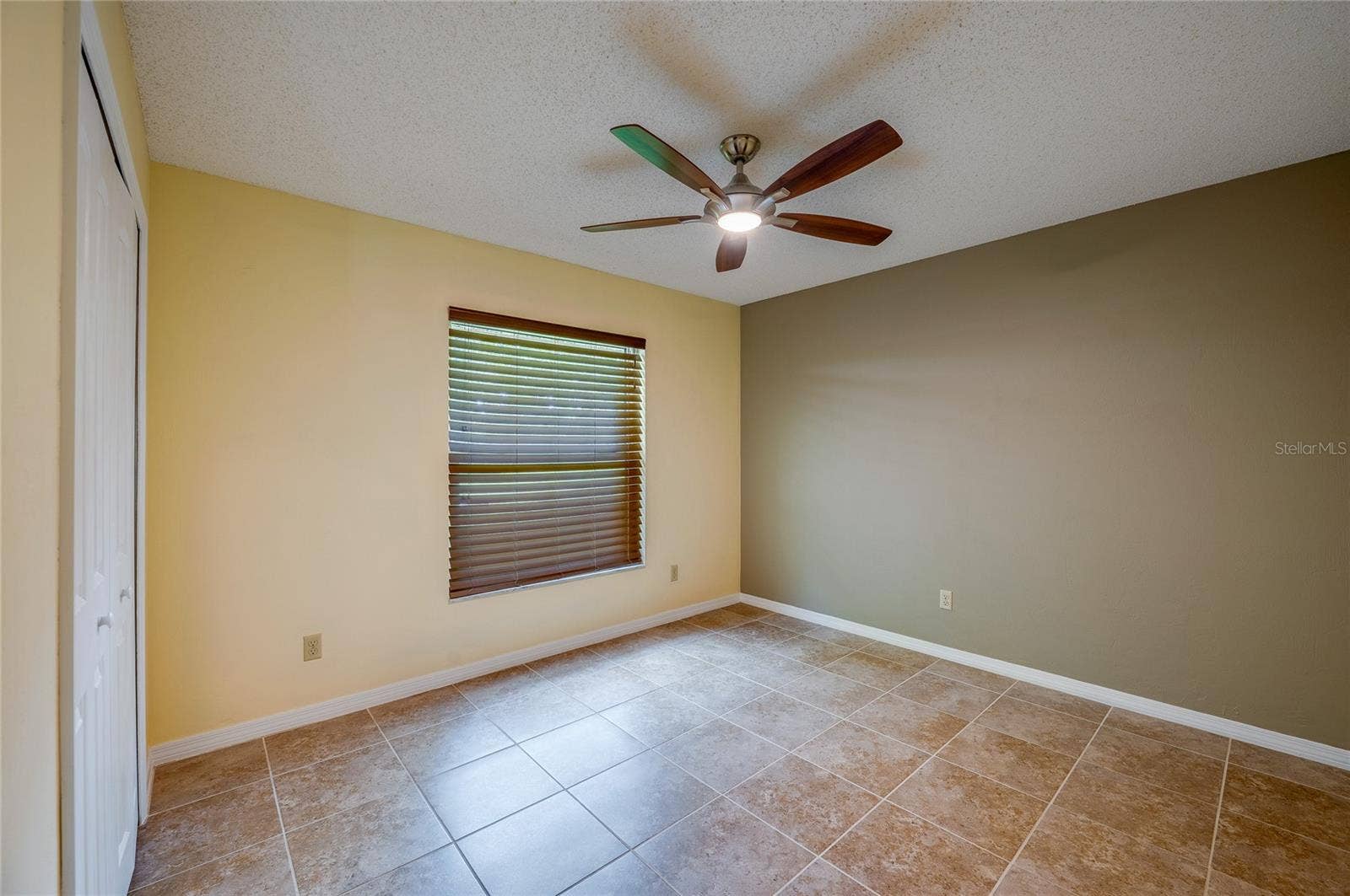 4669 SECRET RIVER TRAIL, Port Orange, FL 32129 Cozy bedroom offering neutral tile floors, warm wall tones, a modern ceiling fan, and built-in closet space. Window blinds provide light control and privacy.