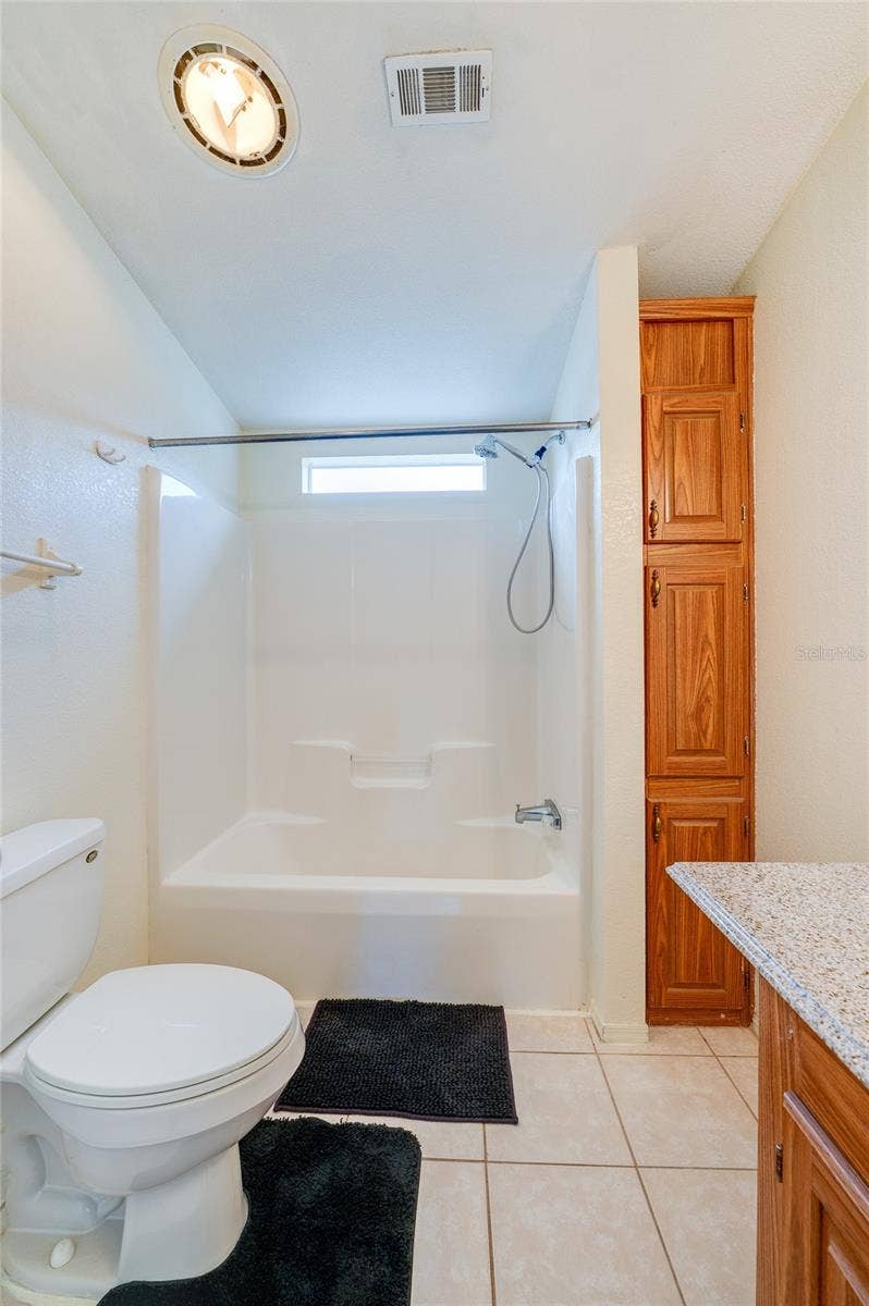 13 LAWRENCE COURT, Port Orange, FL 32127 Additional view highlights the tub-and-shower combination, natural light from a high window, and tall built-in storage cabinetry.
