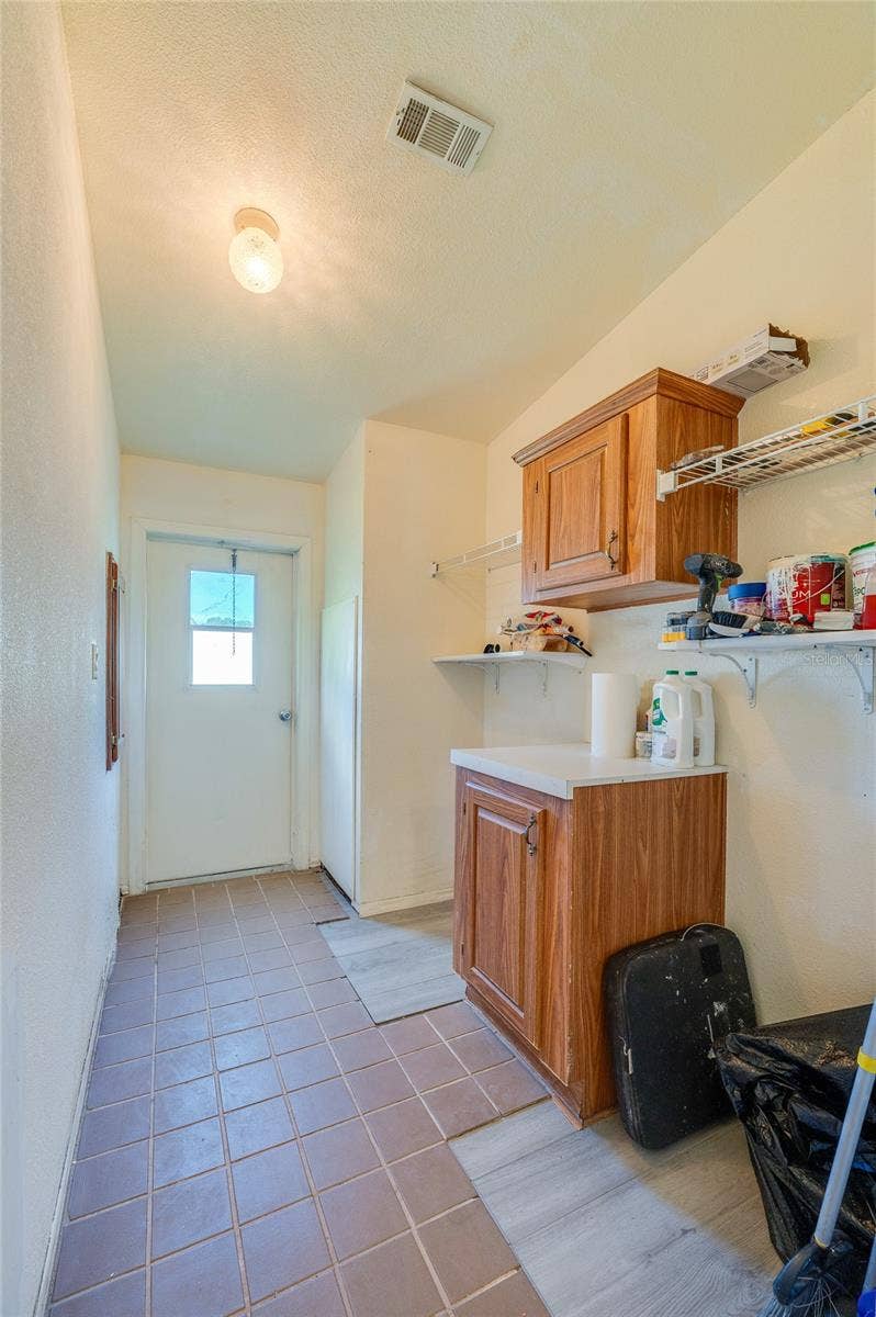 13 LAWRENCE COURT, Port Orange, FL 32127 Functional utility space provides built-in cabinetry, open shelving, counter space, and direct exterior access for added convenience.