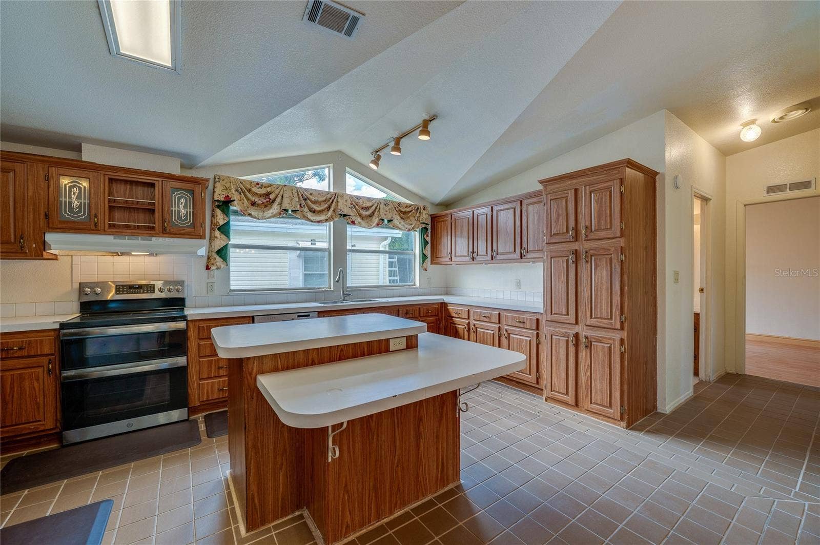 13 LAWRENCE COURT, Port Orange, FL 32127 Another angle showcases the kitchen's generous cabinet storage, center island with multiple work surfaces, large windows, and vaulted architectural detail overhead.