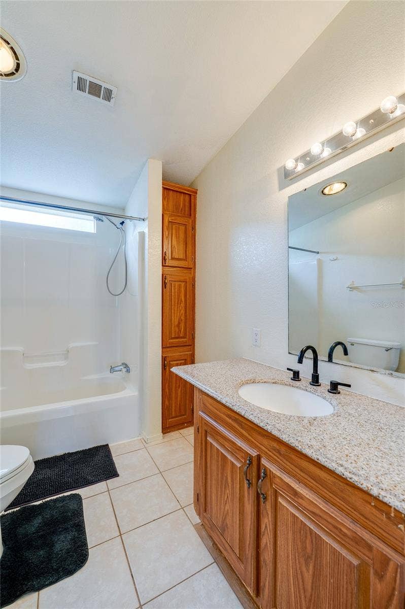 13 LAWRENCE COURT, Port Orange, FL 32127 Full bathroom offers a tub-and-shower combination, vanity with generous counter space, large mirror, tile flooring, and additional built-in storage.