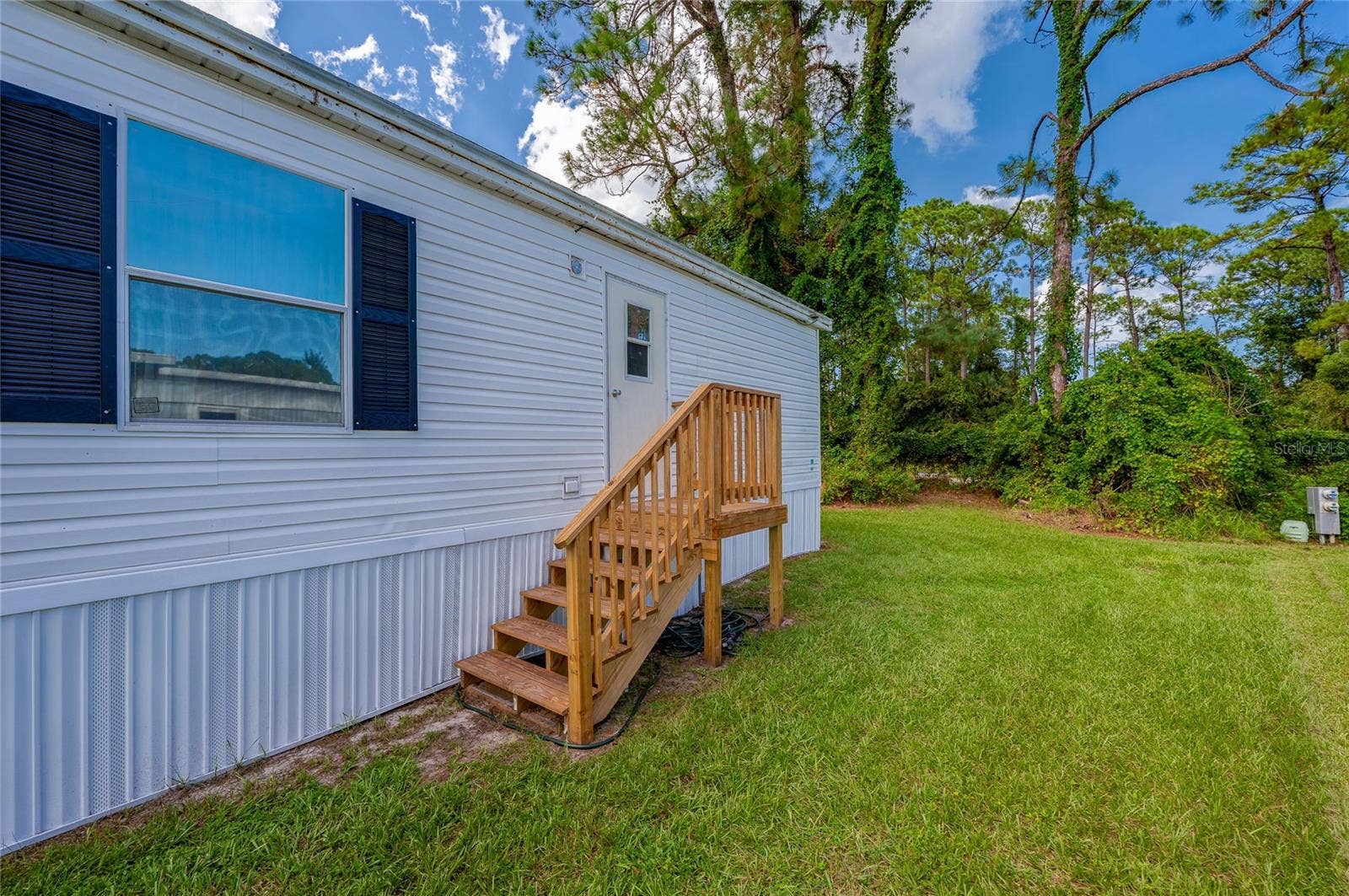 13 LAWRENCE COURT, Port Orange, FL 32127 Rear entry features wood steps with railings leading to the home, opening directly to the surrounding lawn.
