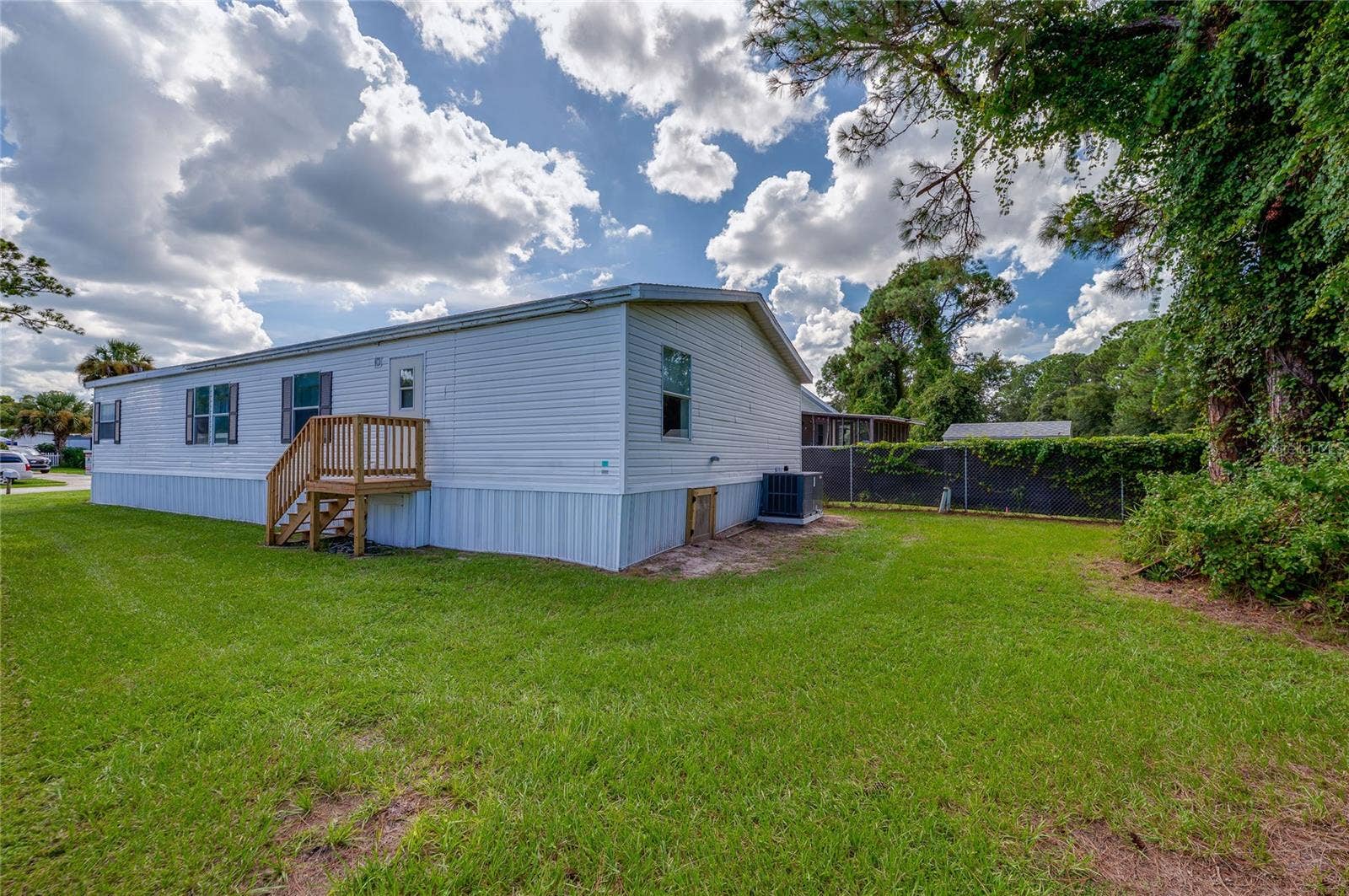 13 LAWRENCE COURT, Port Orange, FL 32127 Wide exterior view showcases the homes rear and side elevations, wood entry steps, open lawn, and mature greenery along the property perimeter.