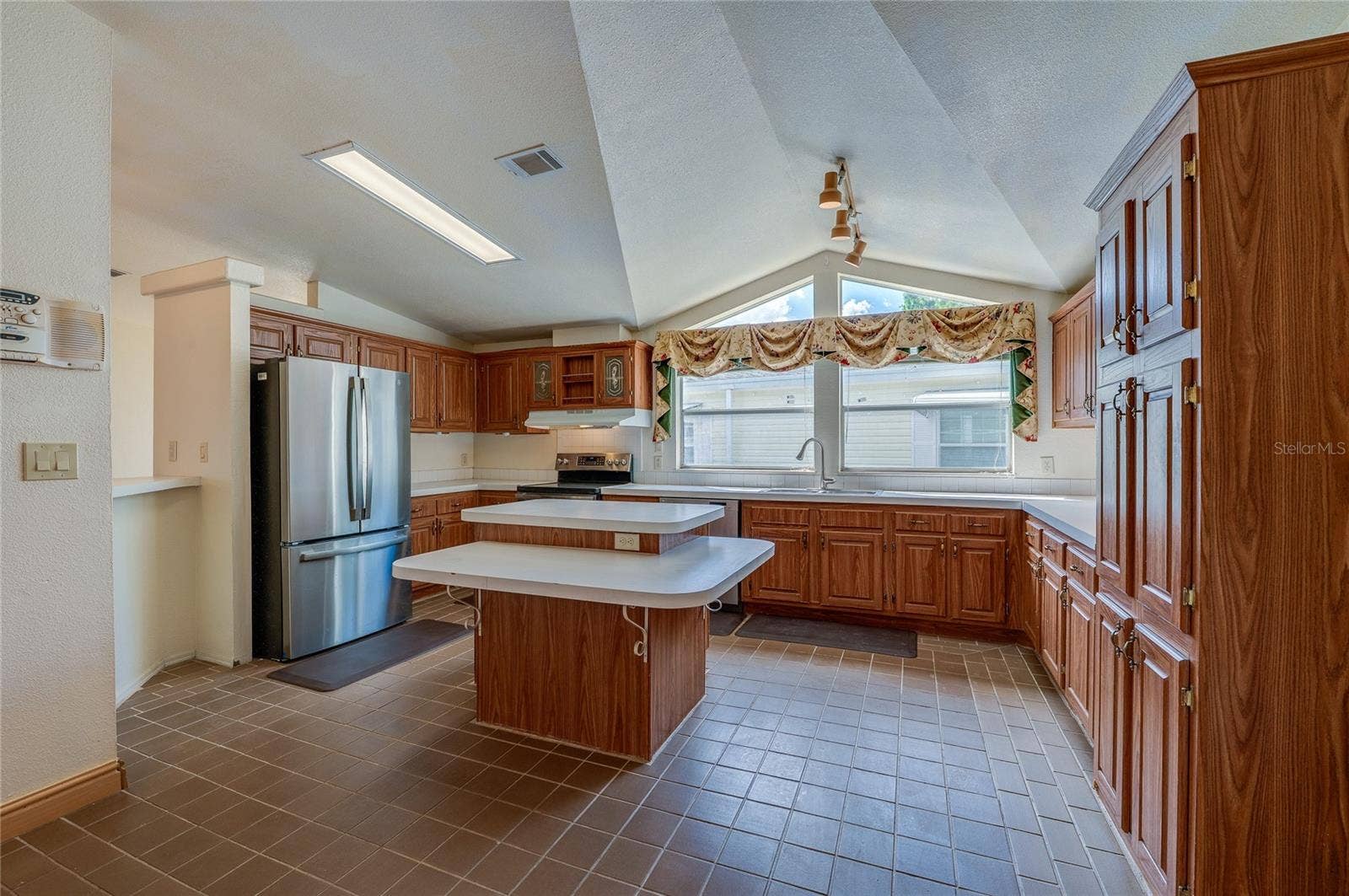 13 LAWRENCE COURT, Port Orange, FL 32127 Spacious kitchen features abundant cabinetry, extensive counter space, a center island, stainless steel refrigerator, and expansive windows beneath a vaulted ceiling.