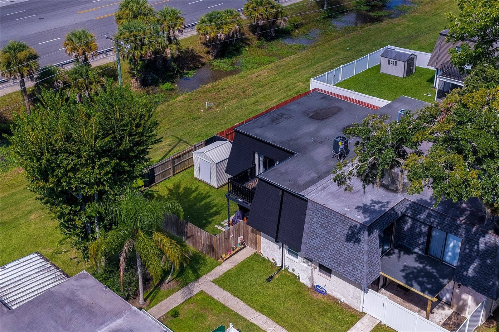 36 SPRINGWOOD SQUARE, Port Orange, FL 32129 Aerial view of a residential property surrounded by lush greenery, featuring fenced yard space, storage shed, and a balcony.