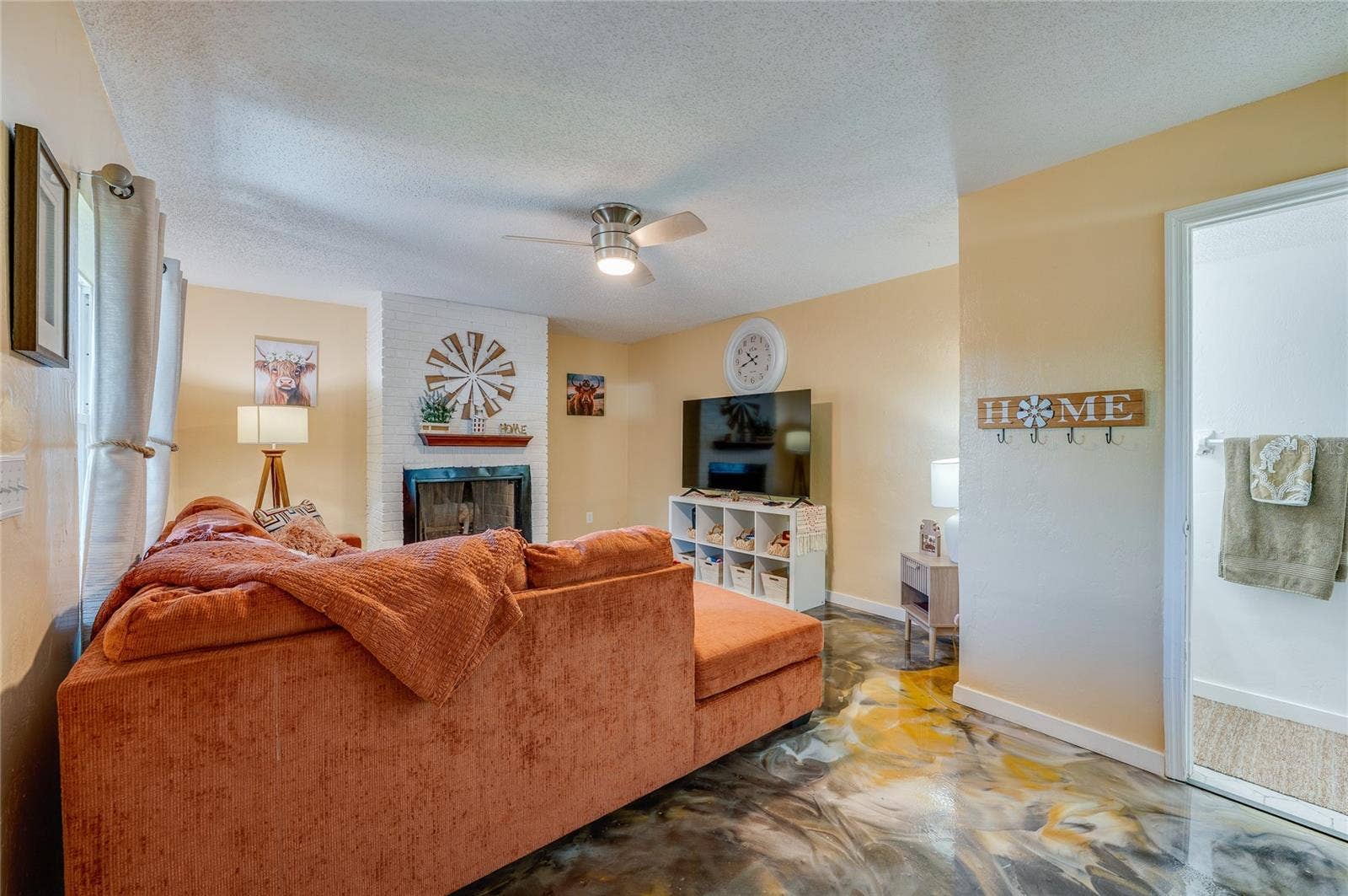 36 SPRINGWOOD SQUARE, Port Orange, FL 32129 Spacious living area showcasing unique epoxy flooring, warm neutral walls, and a white brick accent wall with a fireplace.