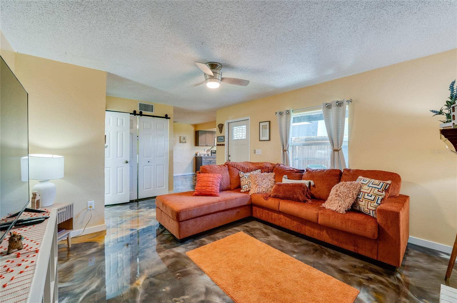 36 SPRINGWOOD SQUARE, Port Orange, FL 32129 Bright living area featuring epoxy floors, a white front entrance door, and sliding closet doors leading to adjoining spaces.