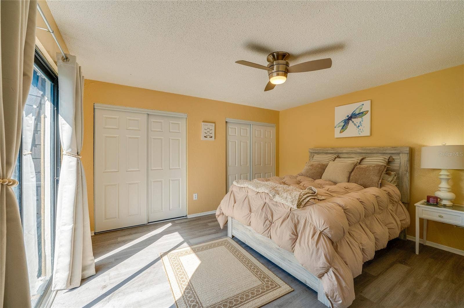 36 SPRINGWOOD SQUARE, Port Orange, FL 32129 Spacious room showcasing LVP flooring, twin closet spaces with white doors, and direct outdoor access via sliding glass doors.