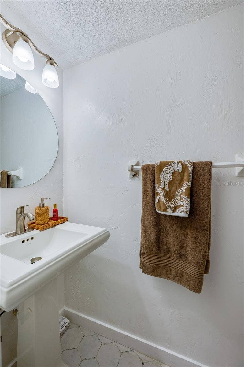 36 SPRINGWOOD SQUARE, Port Orange, FL 32129 Compact half-bathroom with a white pedestal sink, rounded wall mirror, and modern lighting fixture.