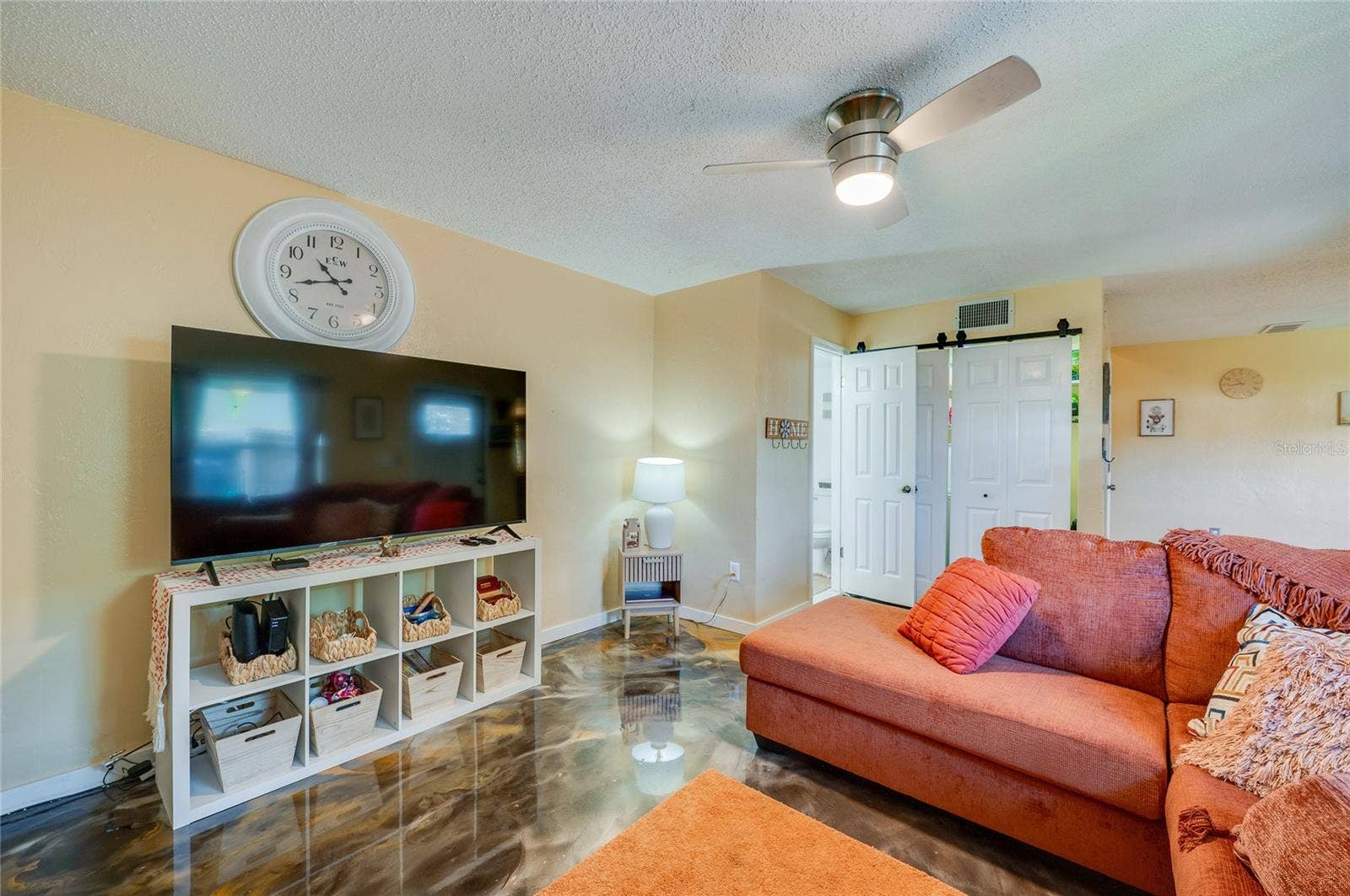 36 SPRINGWOOD SQUARE, Port Orange, FL 32129 Inviting living space highlights striking epoxy floor finishes, a ceiling fan, and white sliding barn doors for a modern touch.