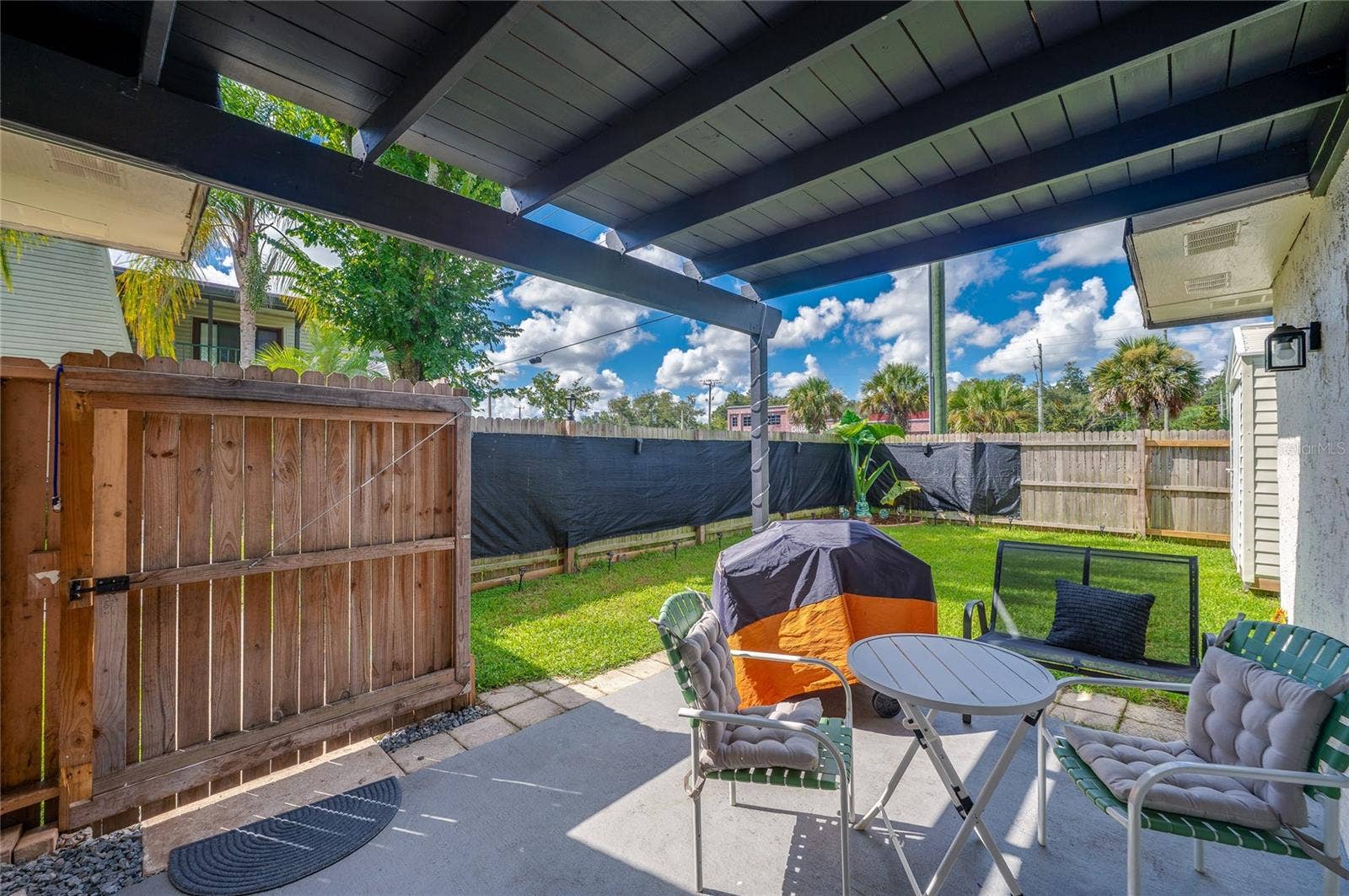 36 SPRINGWOOD SQUARE, Port Orange, FL 32129 Covered ground-floor patio leading out to a fully fenced private yard framed by lush green grass.