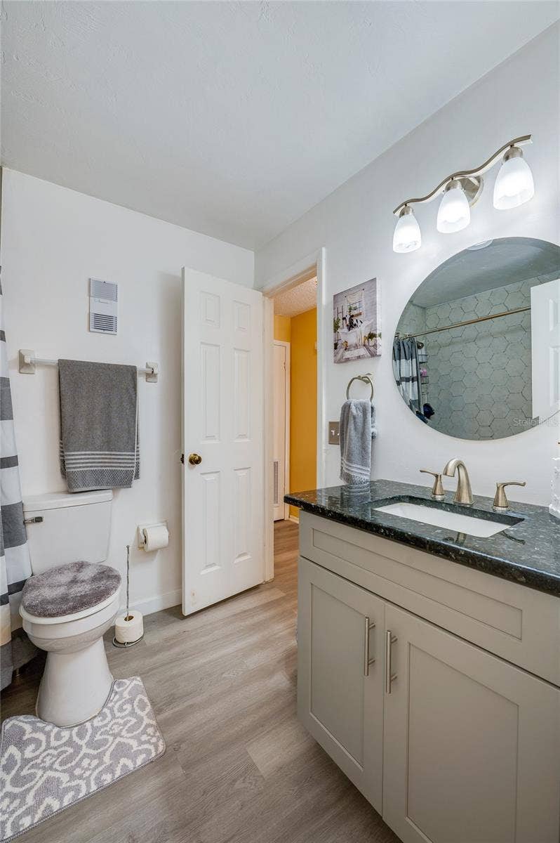36 SPRINGWOOD SQUARE, Port Orange, FL 32129 Full bathroom featuring a vanity with dark granite countertops, LVP flooring, and a circular wall mirror.