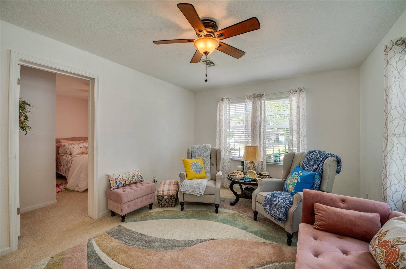 60 GOLDEN GATE CIRCLE, Port Orange, FL 32129 Light-filled room featuring plush carpeting, a center ceiling fan, and large windows that overlook the outdoors. An open doorway provides smooth access to an adjoining bedroom space.