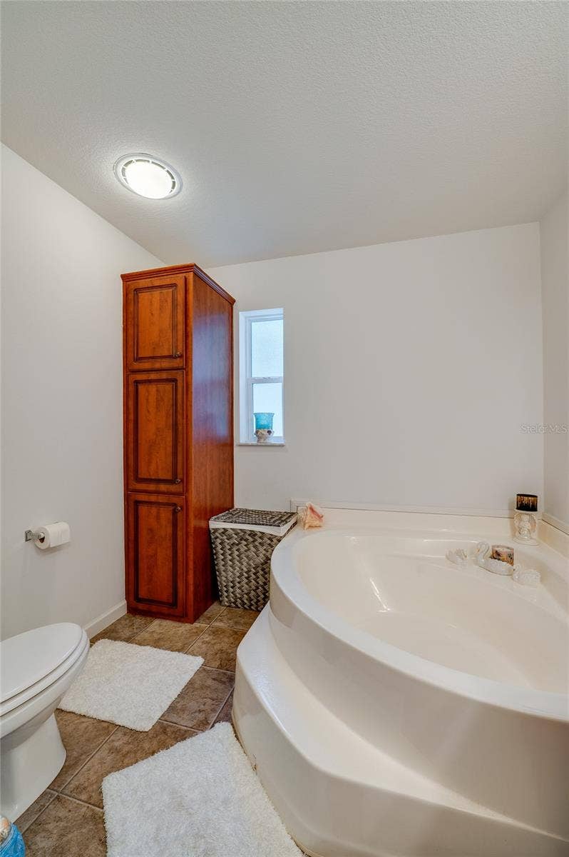 60 GOLDEN GATE CIRCLE, Port Orange, FL 32129 Bathroom corner highlighting a deep corner soaking tub, tall wood linen cabinet, and tile flooring lit by overhead recessed lighting.