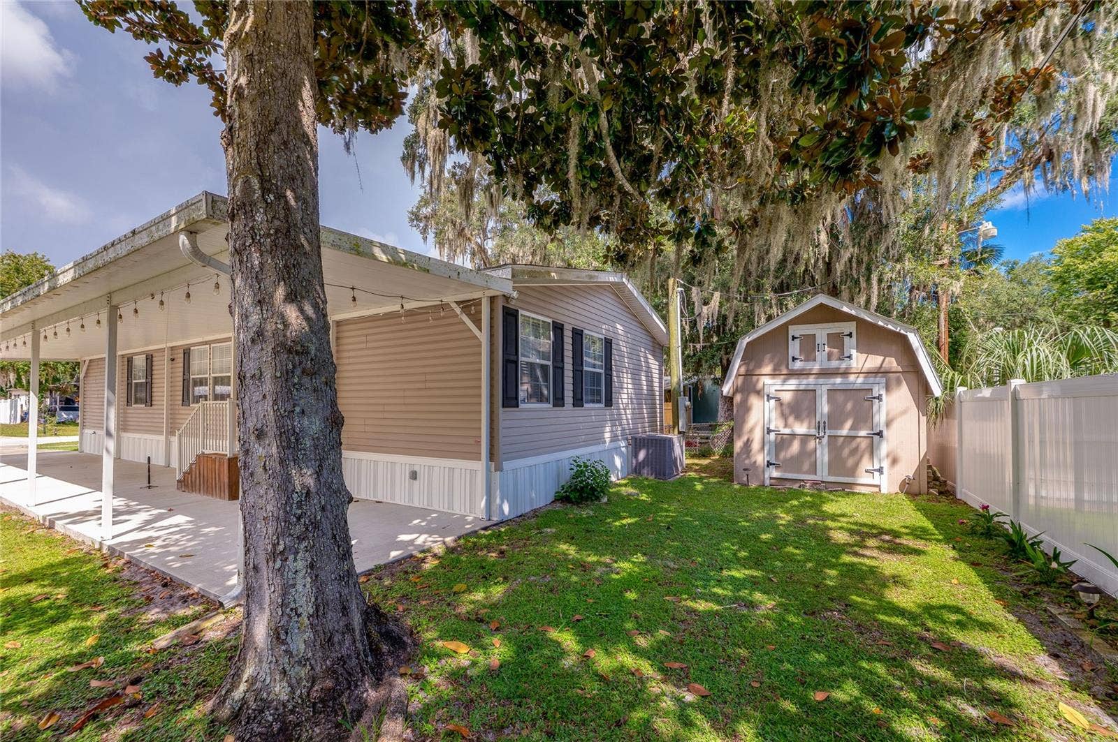 60 GOLDEN GATE CIRCLE, Port Orange, FL 32129 Side view of the home featuring an expansive covered carport, attached exterior lighting, and direct access to the lawn and storage shed.