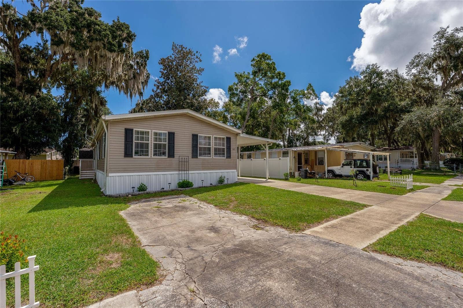 60 GOLDEN GATE CIRCLE, Port Orange, FL 32129 Exterior view of the home featuring neutral siding, dark window shutters, a paved driveway, and surrounding green lawn.