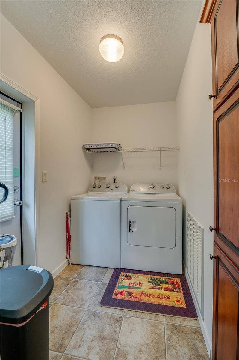 60 GOLDEN GATE CIRCLE, Port Orange, FL 32129 Dedicated laundry room offering full-size washer and dryer units with built-in wire shelving above. The room features easy-to-clean linoleum flooring and an exterior access door.