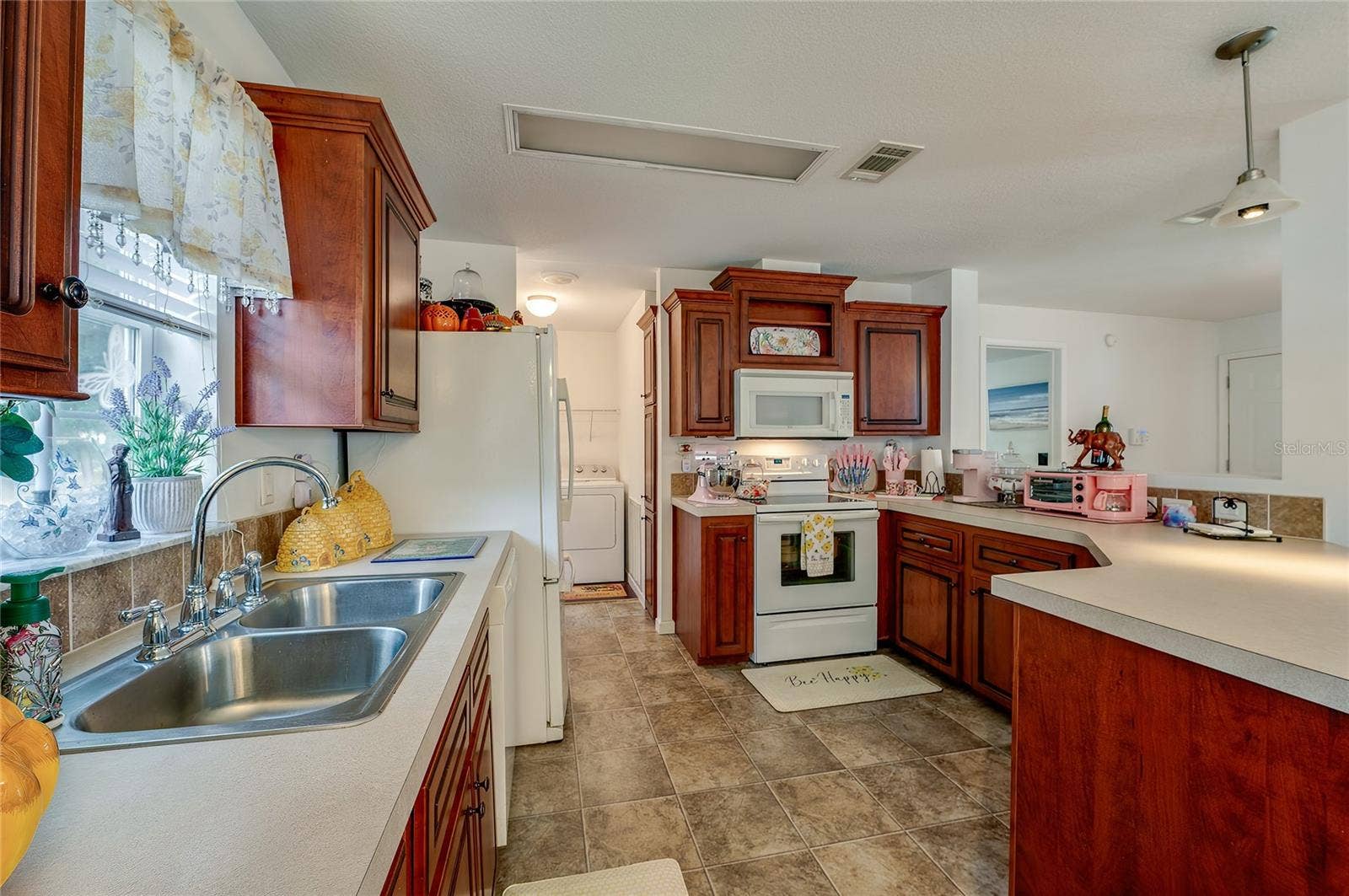 60 GOLDEN GATE CIRCLE, Port Orange, FL 32129 Functional kitchen space equipped with full-size white appliances, a double-basin stainless steel sink, and rich wood cabinetry. Durable linoleum flooring and generous counter space make for an efficient workspace.